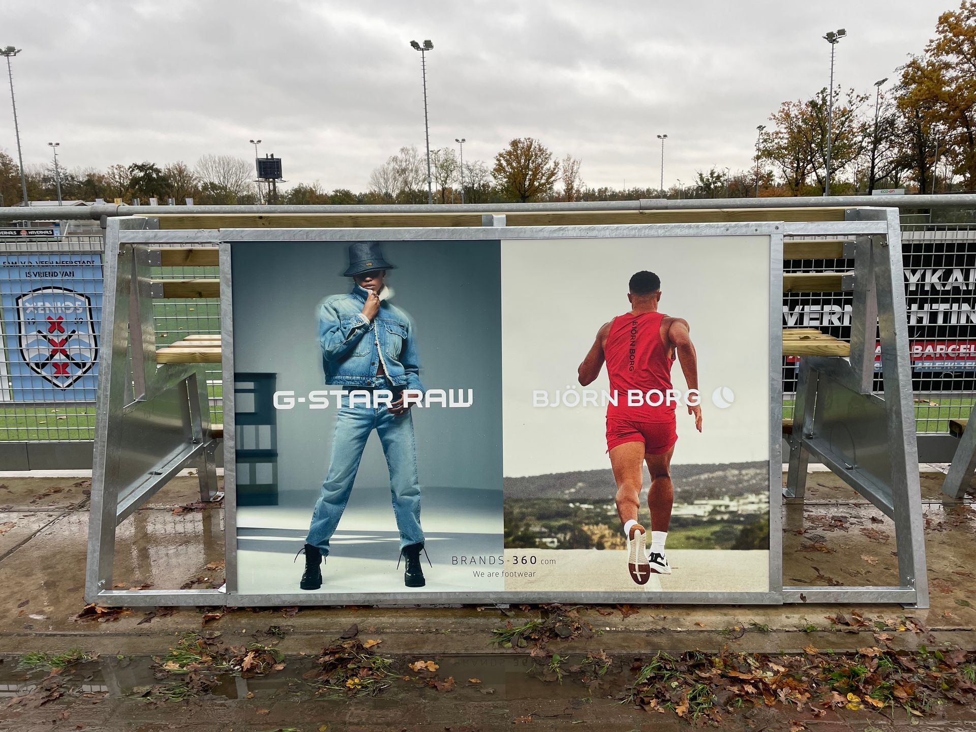 Buitenreclame met de logo's van G-Star Raw en Bjorn Borg, naast elkaar op een Fanseats bank bij een hockey club.