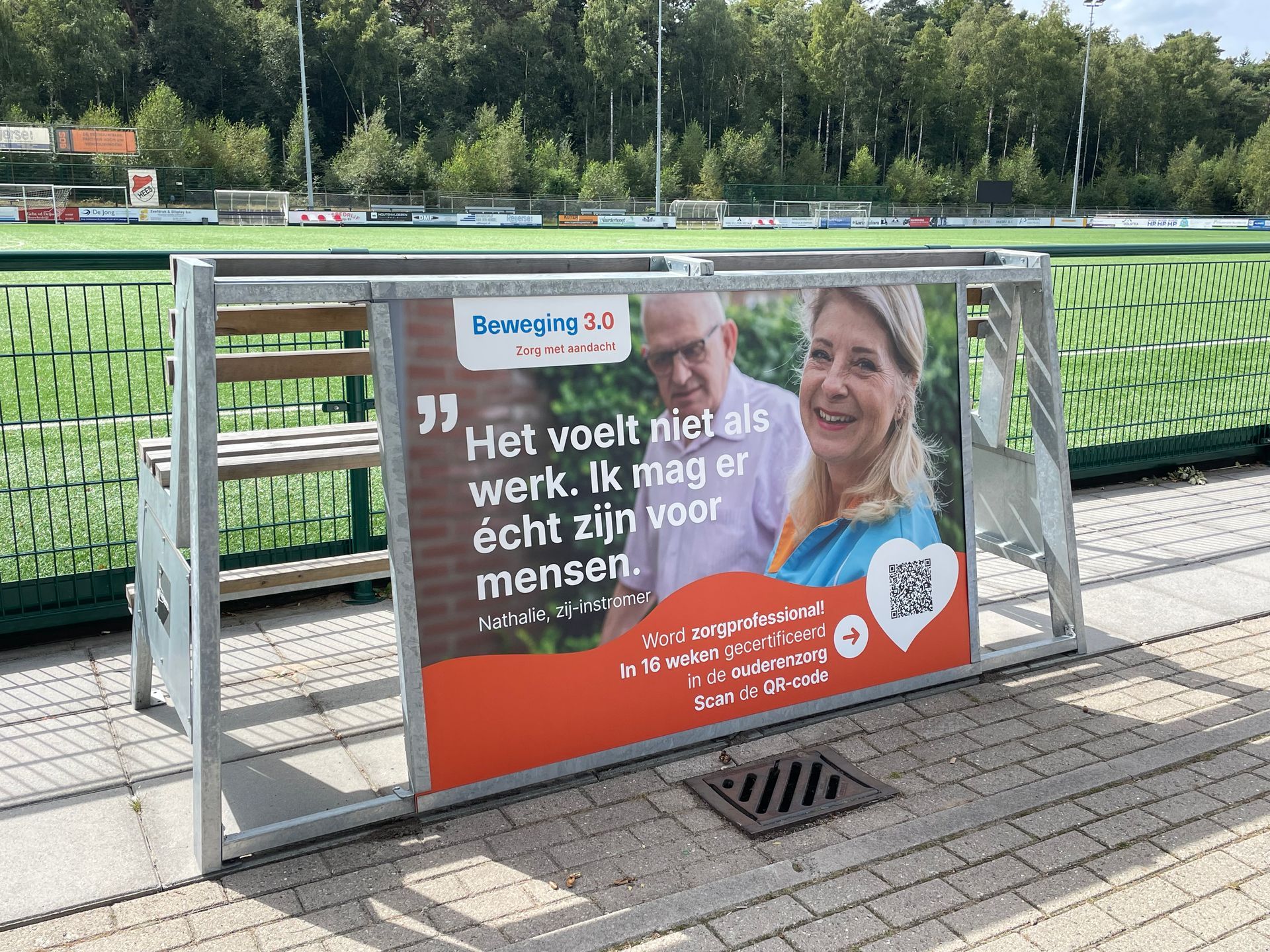 Fanseats bank langs het hockeyveld met reclame. Tekst: 