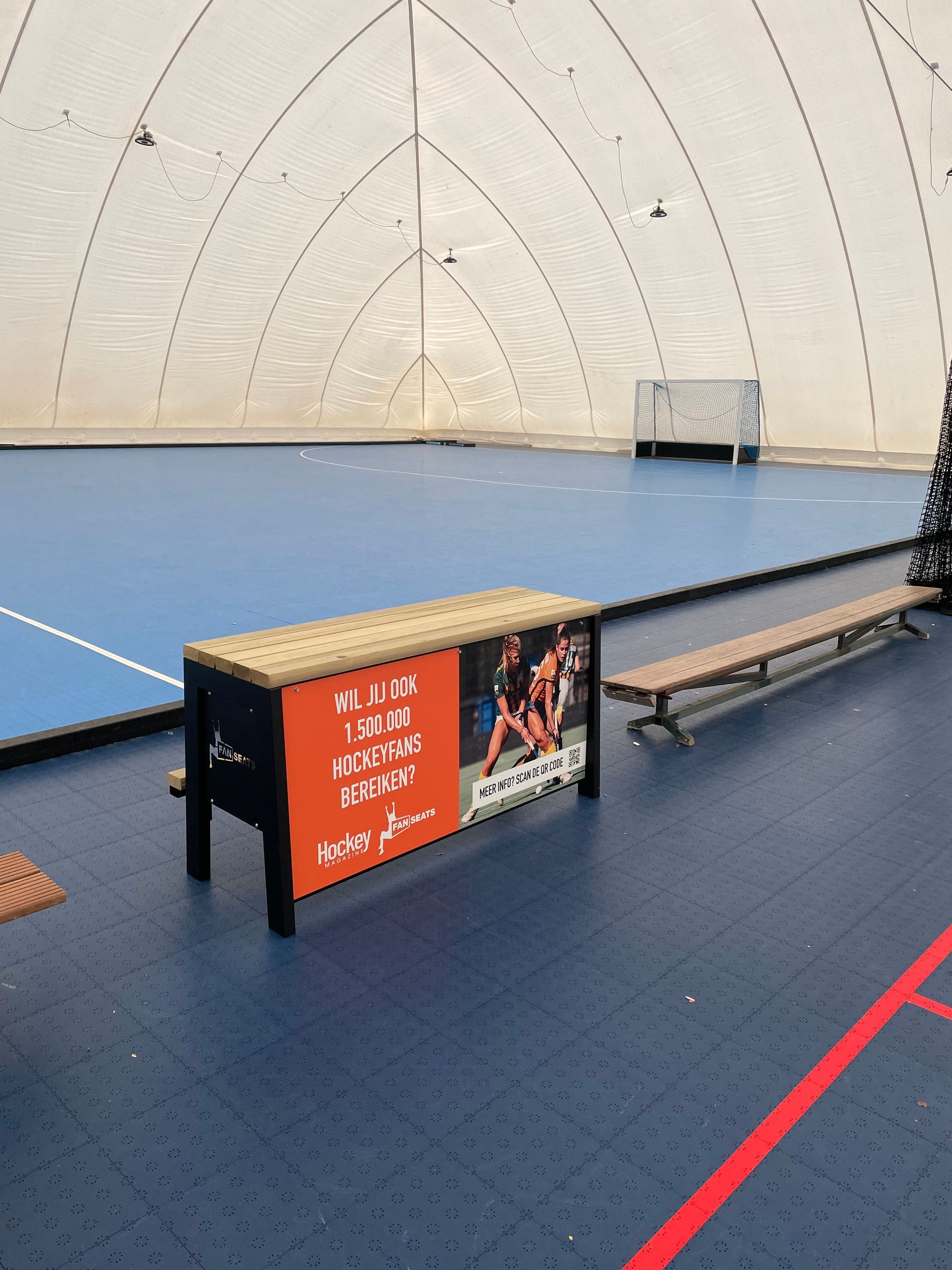 Een indoor sportveld met een blauwe vloer, banken voor het sportveld waarin reclame kan worden geplaatst