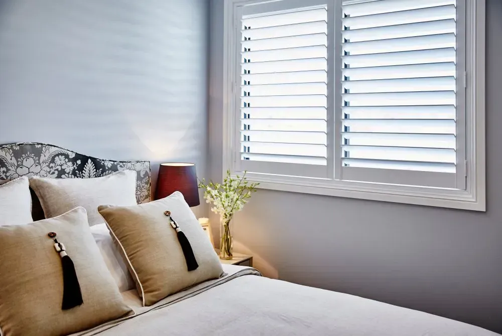 A Bedroom With A Bed And A Window With Shutters — Coastal Blind Installations In Agnes Waters, QLD