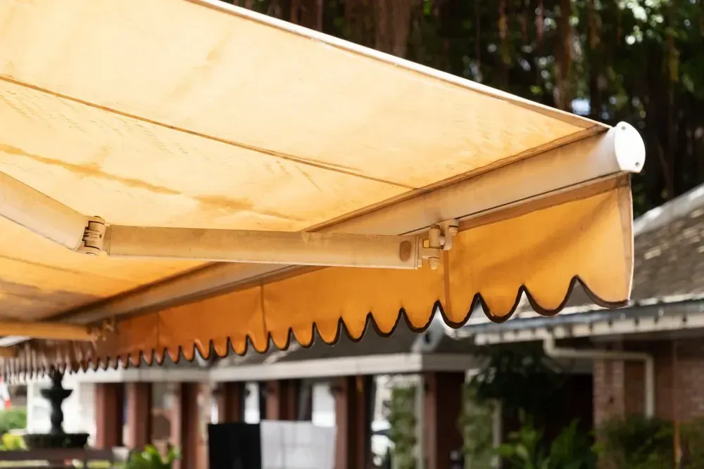 A Yellow Awning Is Hanging From The Side Of A Building — Coastal Blind Installations In Bargara, QLD