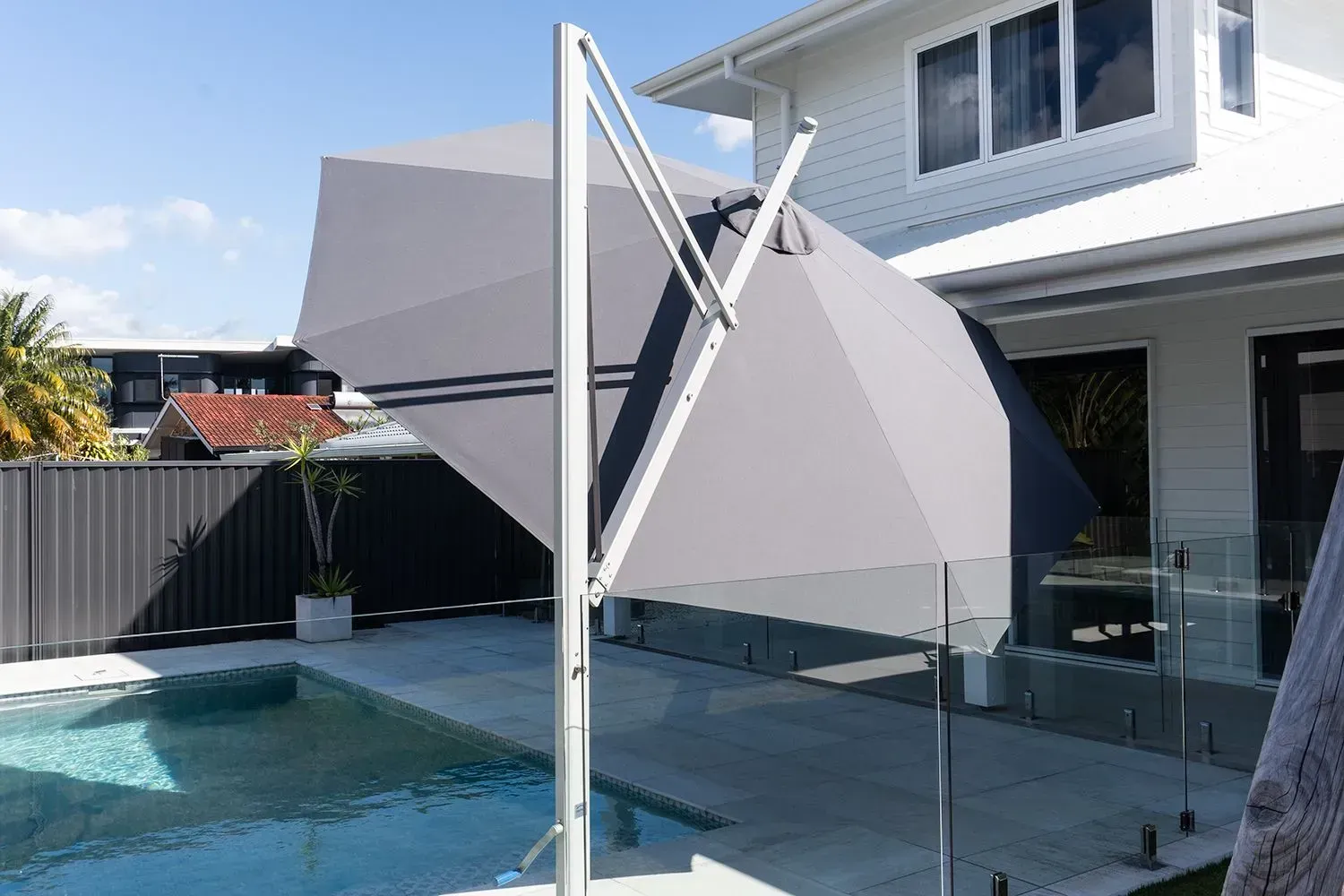 A Large Umbrella Is Sitting Next To A Swimming Pool In Front Of A House — Coastal Blind Installations In Agnes Waters, QLD