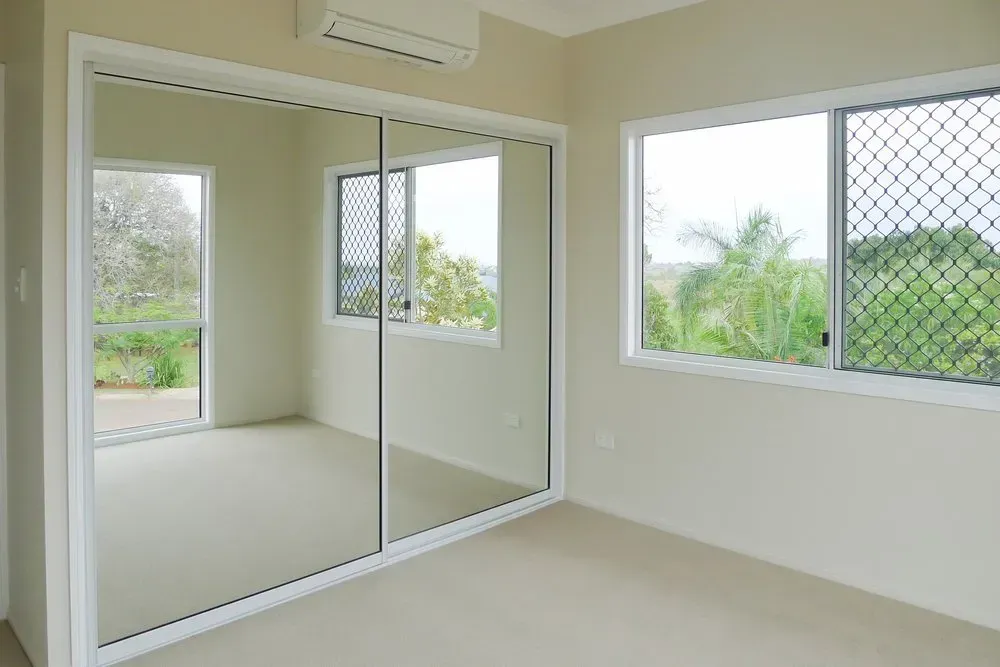 An Empty Bedroom With Sliding Mirrored Doors And Two Windows — Coastal Blind Installations In Bargara, QLD