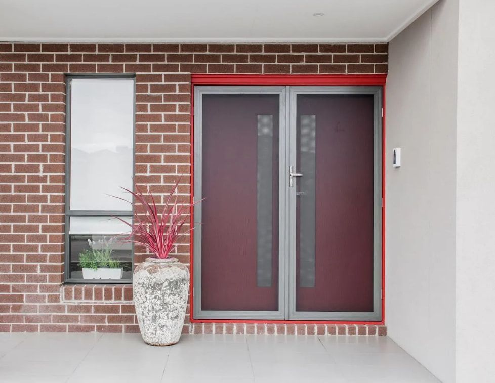 A Brick Building With A Red Door And A Potted Plant In Front Of It — Coastal Blind Installations In Kensington, QLD