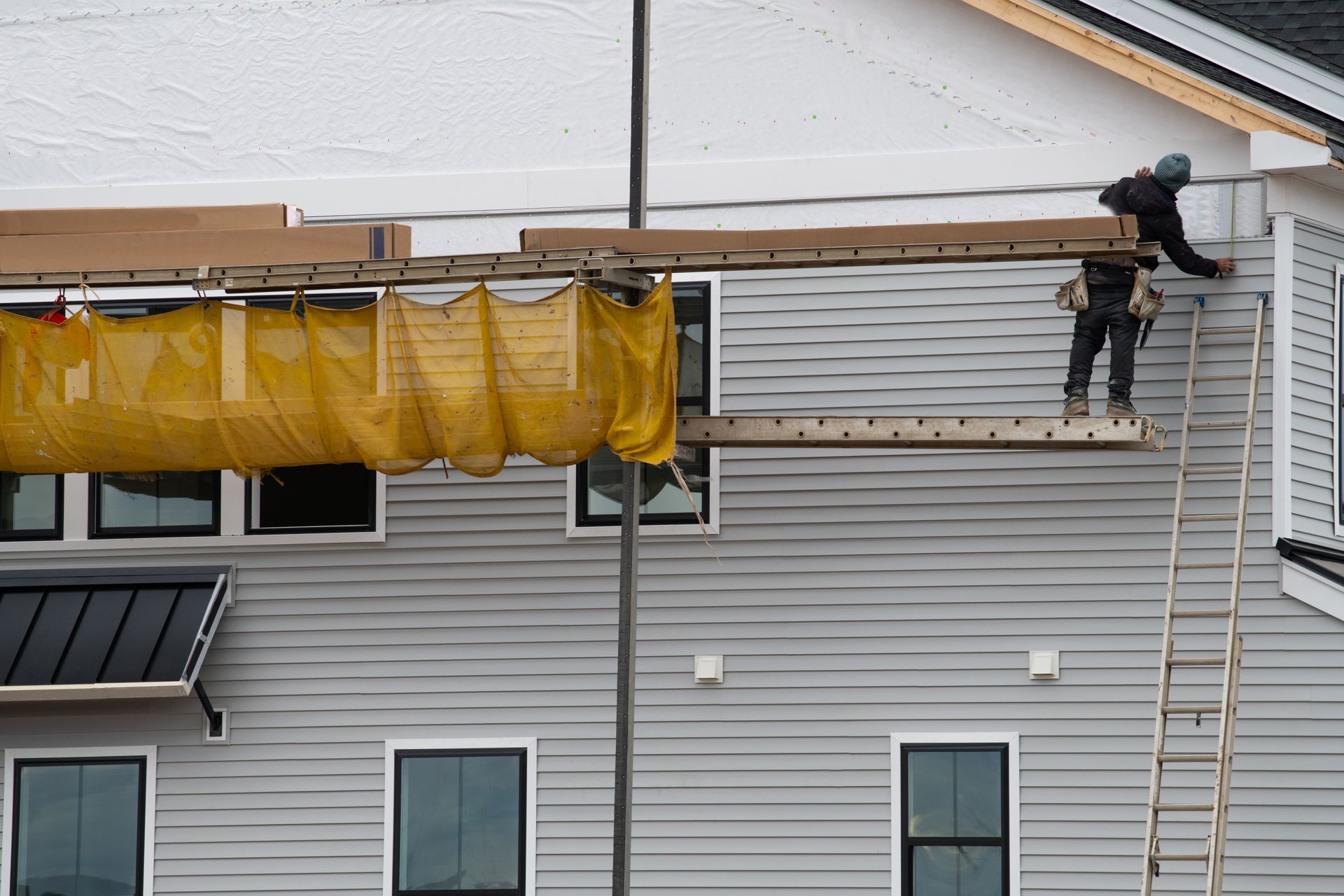 Worker installing siding on a modern residential home, ensuring durability and proper alignment. Worker installing siding on a modern residential home, ensuring durability and proper alignment.
