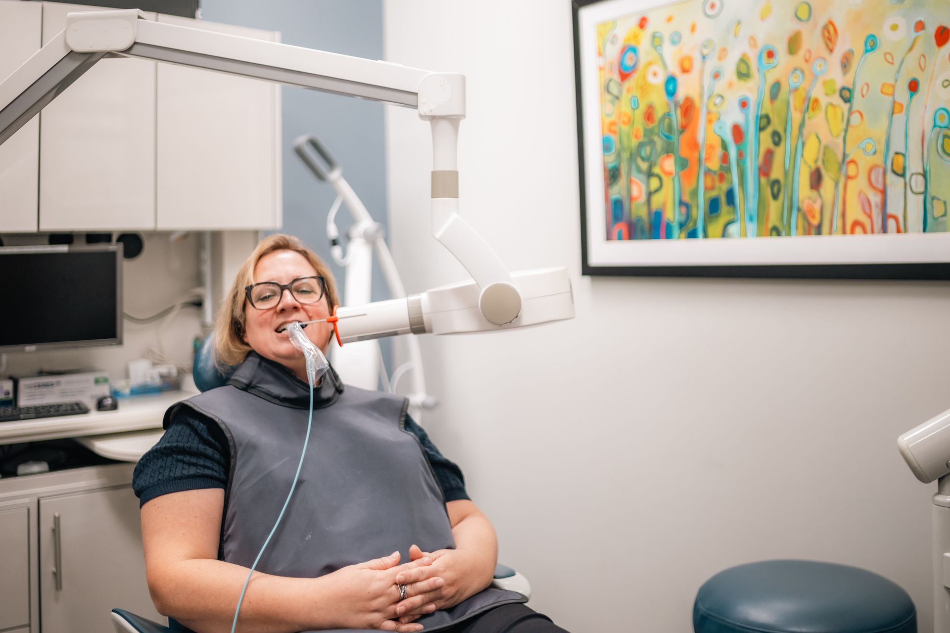 A woman is sitting in a dental chair getting an x-ray of her teeth.
