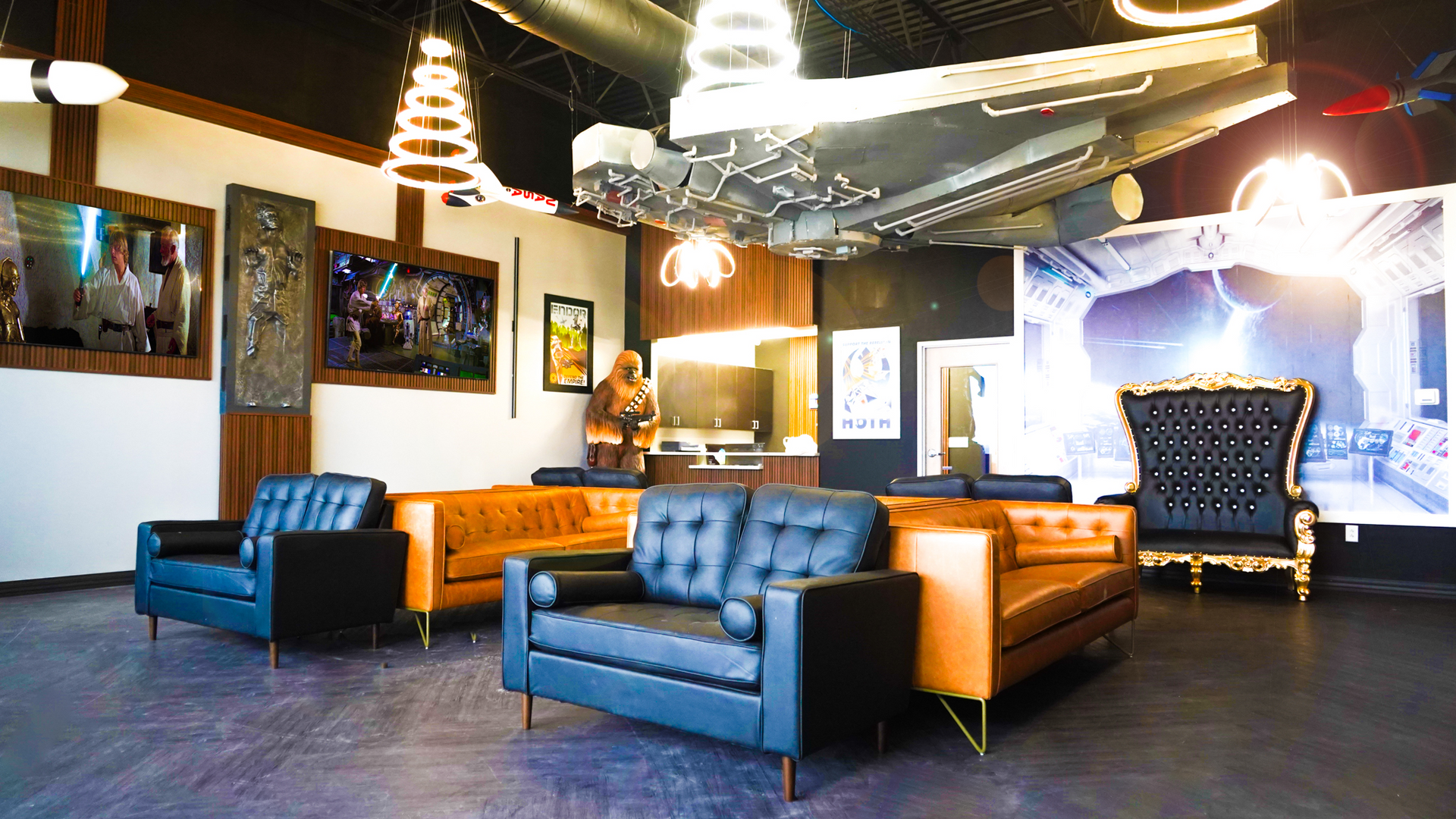 A modern lounge featuring a model Millennium Falcon on the ceiling, leather sofas, armchairs, and a large throne chair.