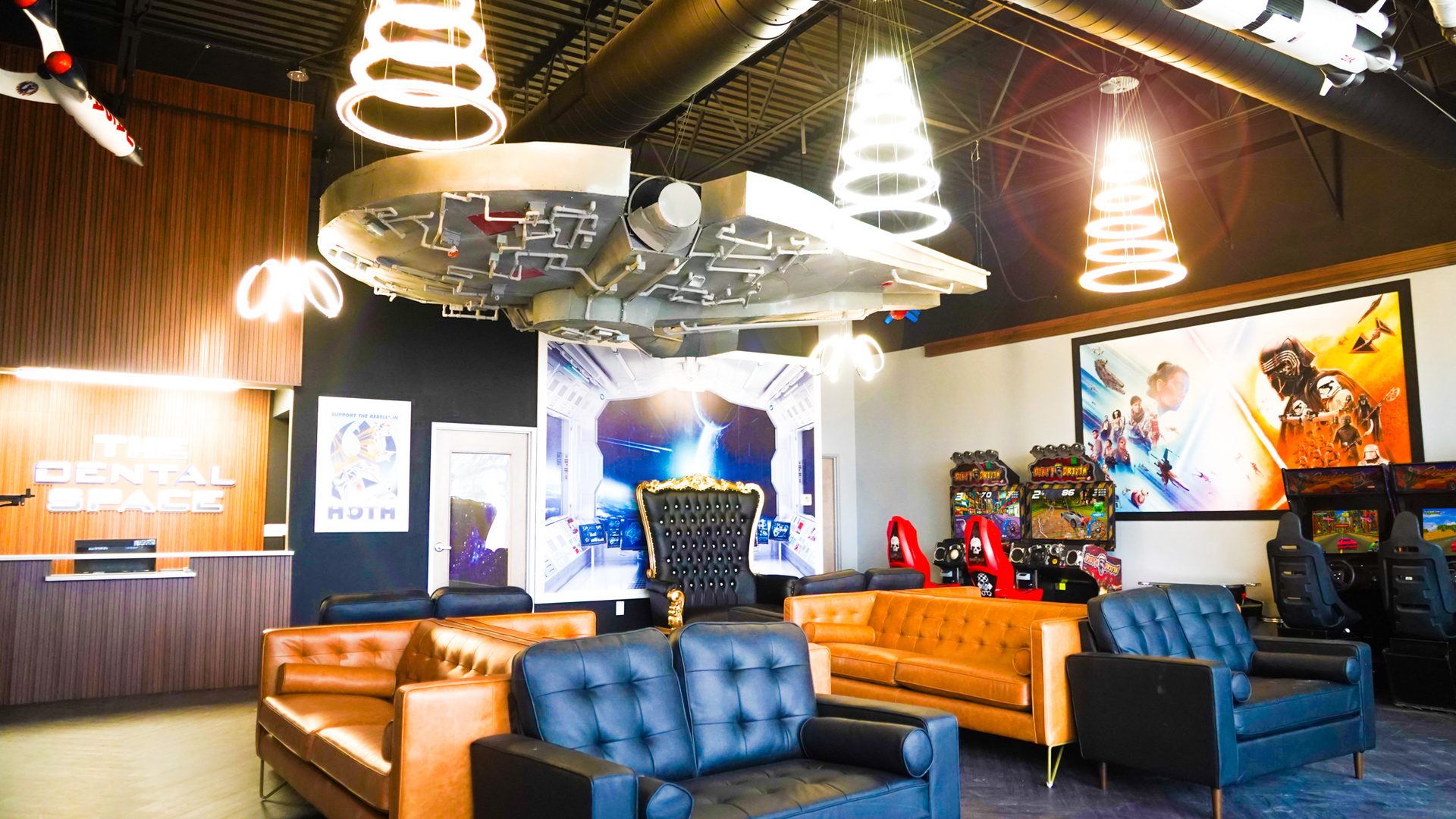 A waiting room styled like a spaceship with leather couches, arcade machines, and a Millennium Falcon model on the ceiling.