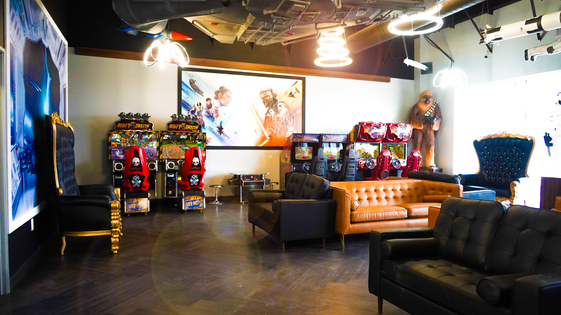 A Star Wars-themed lounge featuring arcade games, leather sofas, high-backed chairs, and a ceiling-mounted Millennium Falcon.