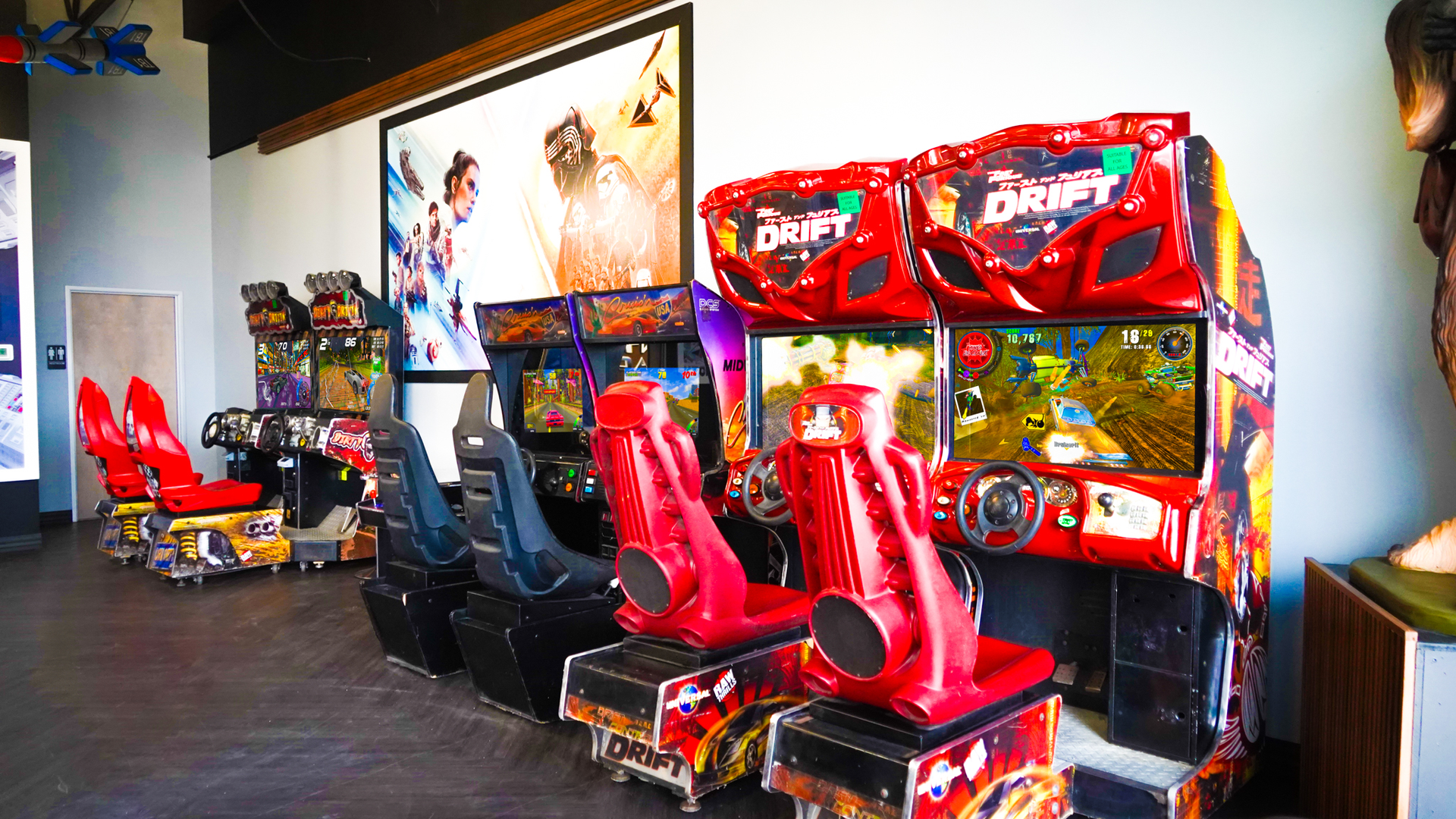 A row of red and blue arcade racing game machines in an indoor game room.