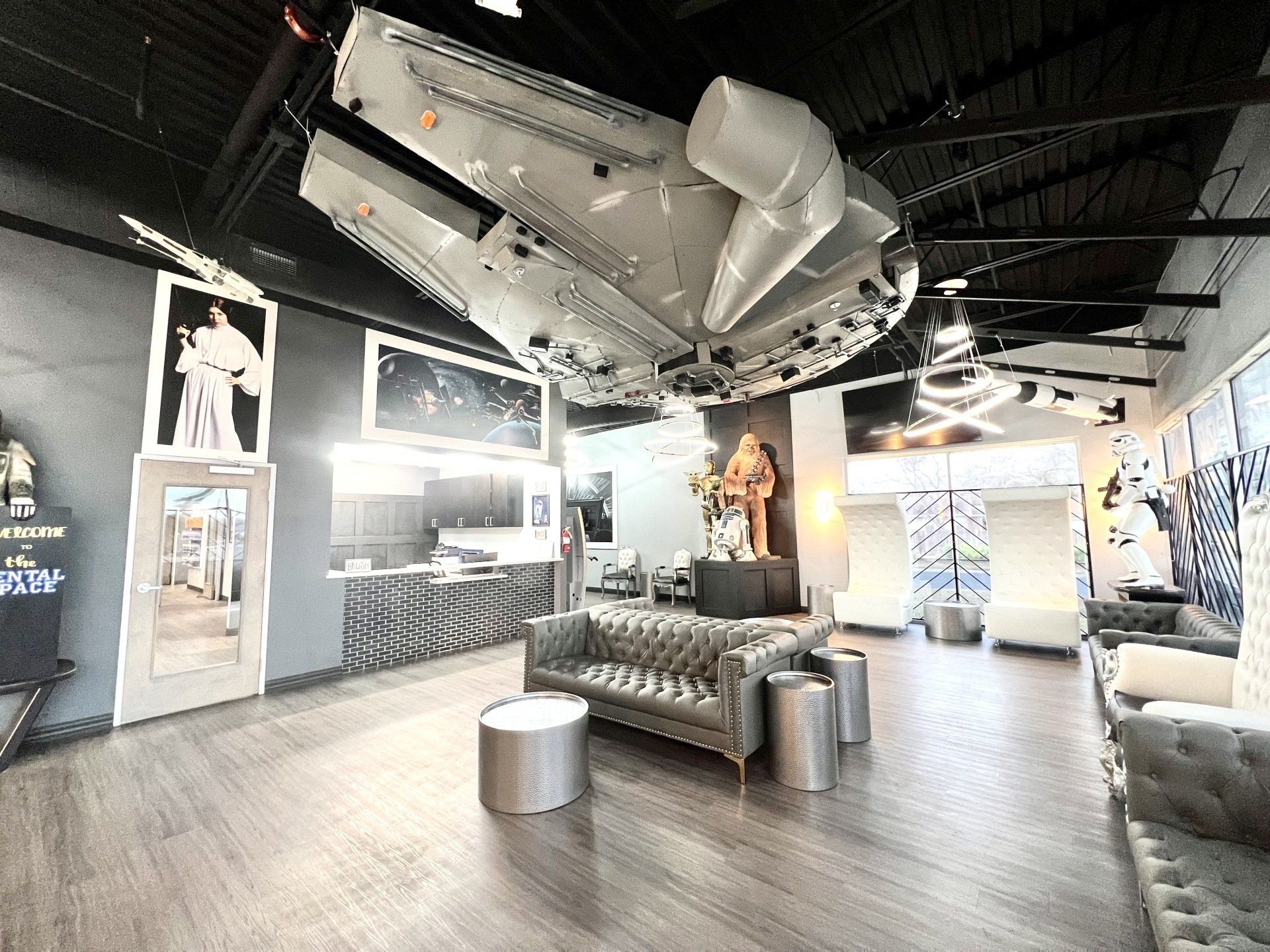 A Star Wars-themed lobby featuring a ceiling-mounted Millennium Falcon, grey tufted sofas, and film-inspired decor.