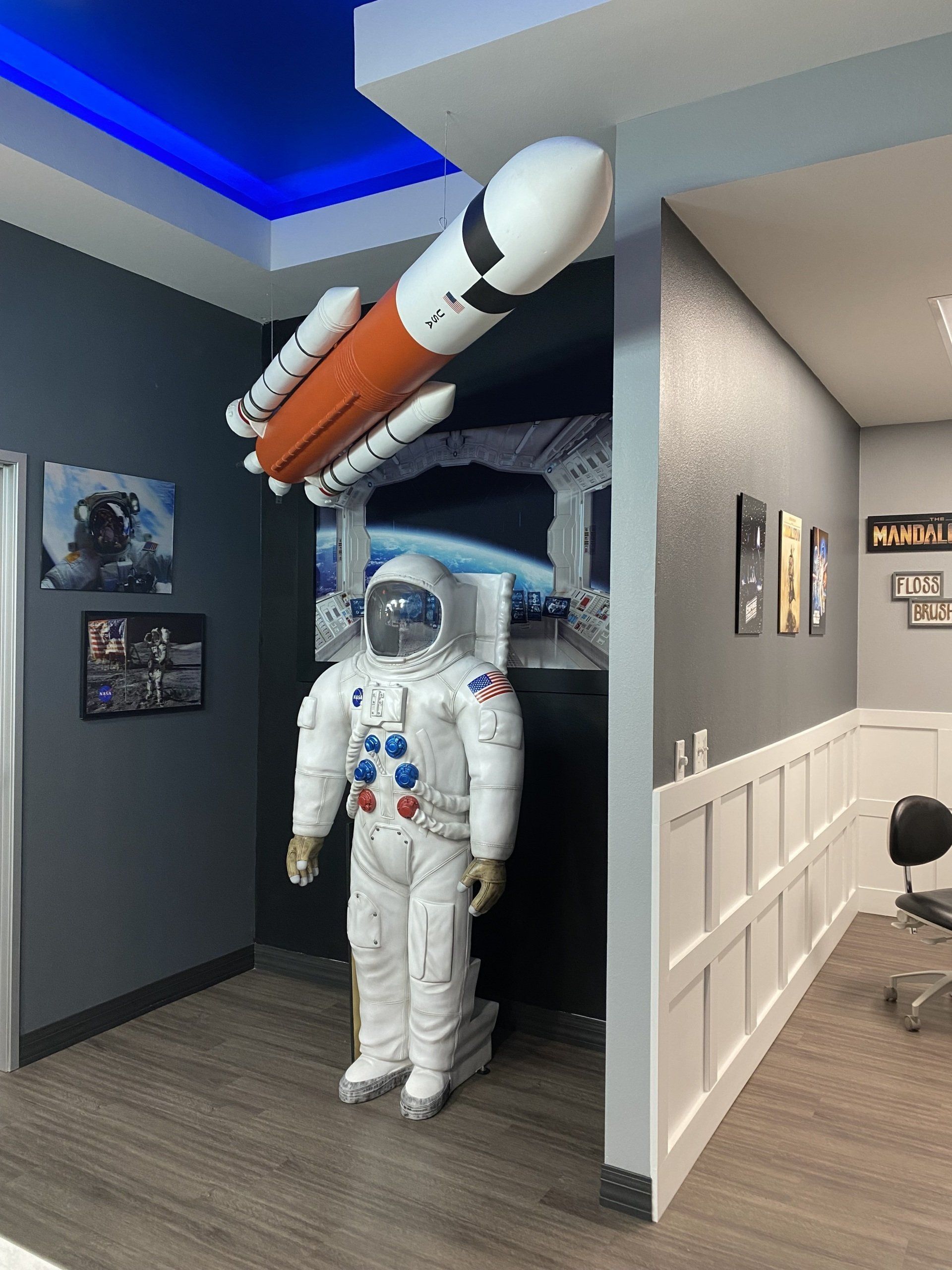 A full-sized astronaut figure stands in a room decorated with a model space shuttle and wall art of outer space.