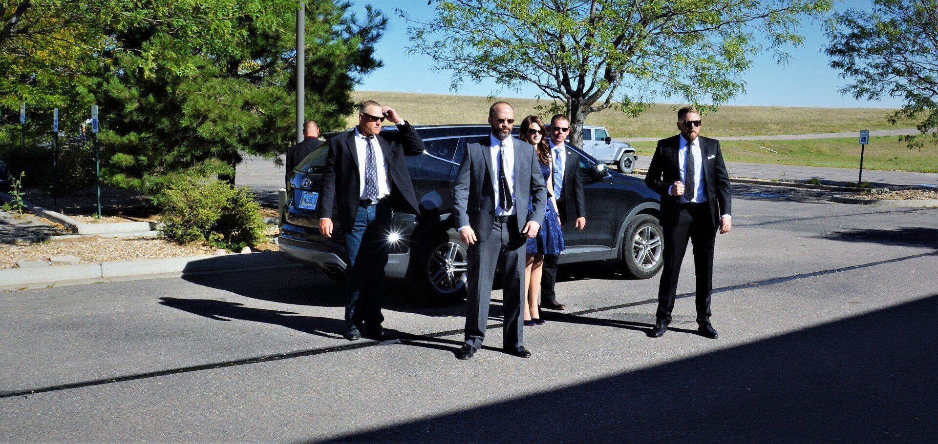 A group of men in suits and ties are standing in front of a car.