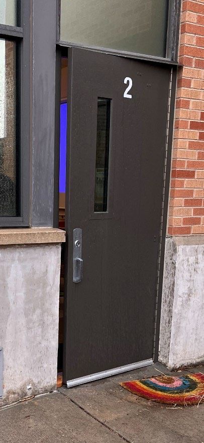 A door with the number 2 on it is open to a brick building.
