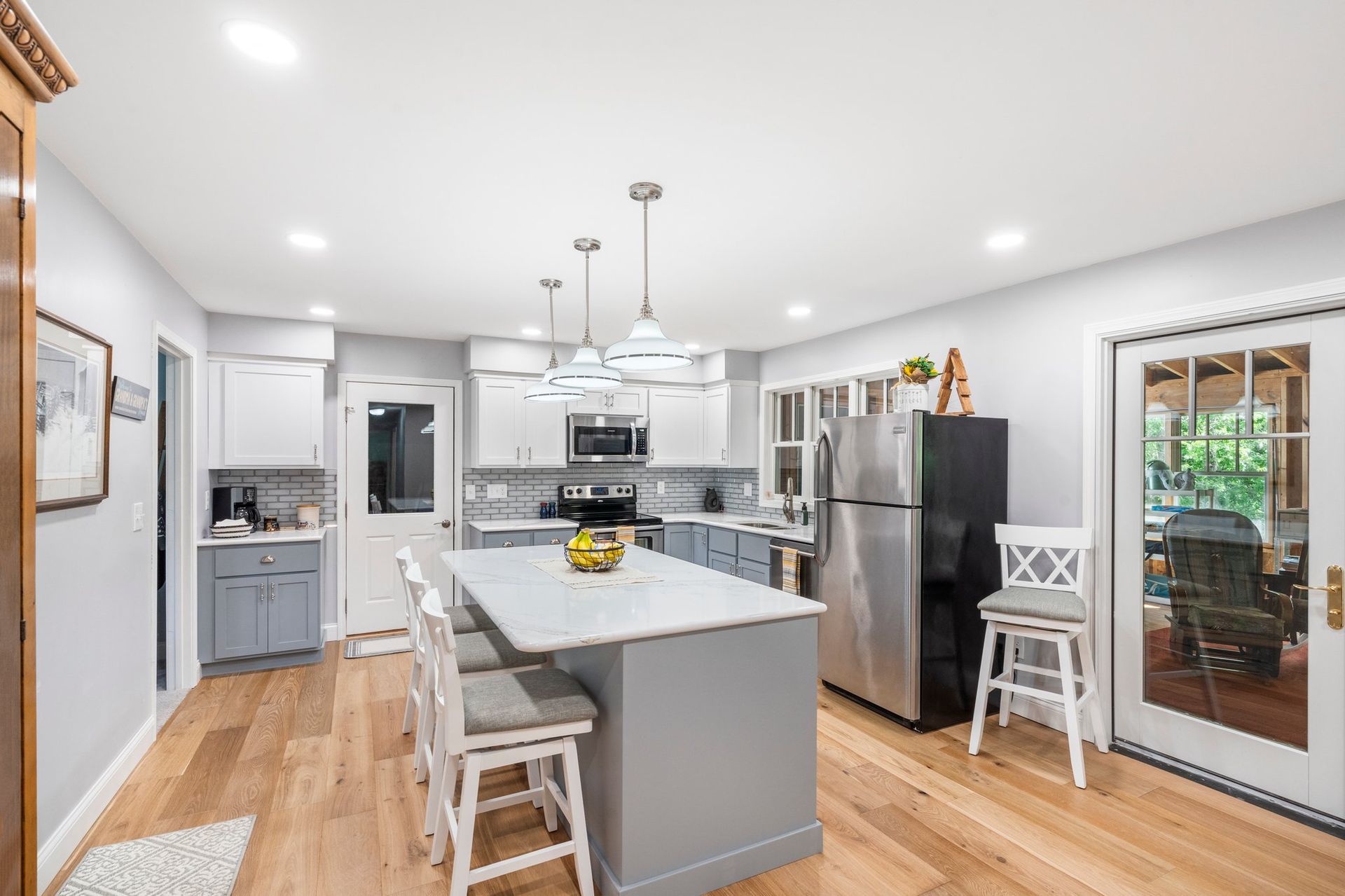 Modern kitchen with gray island, white cabinets, stainless steel appliances, and hardwood floors.