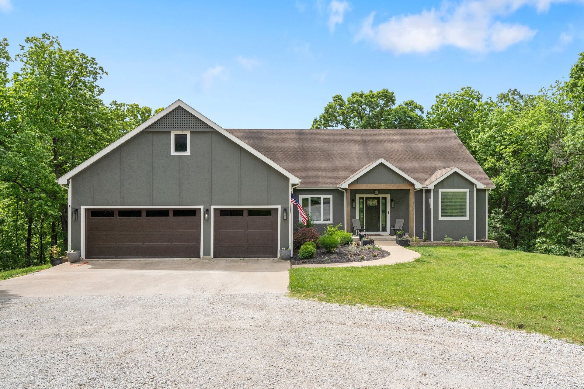 Gray house with brown garage doors, gravel driveway, and green lawn.