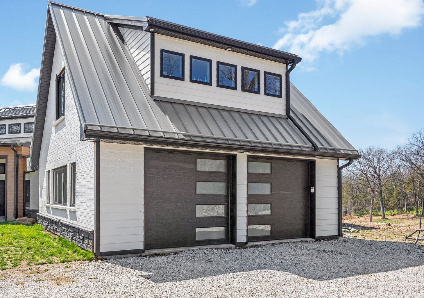 Two-car garage with a metal roof and modern design. White siding, black trim, and clear garage door windows.
