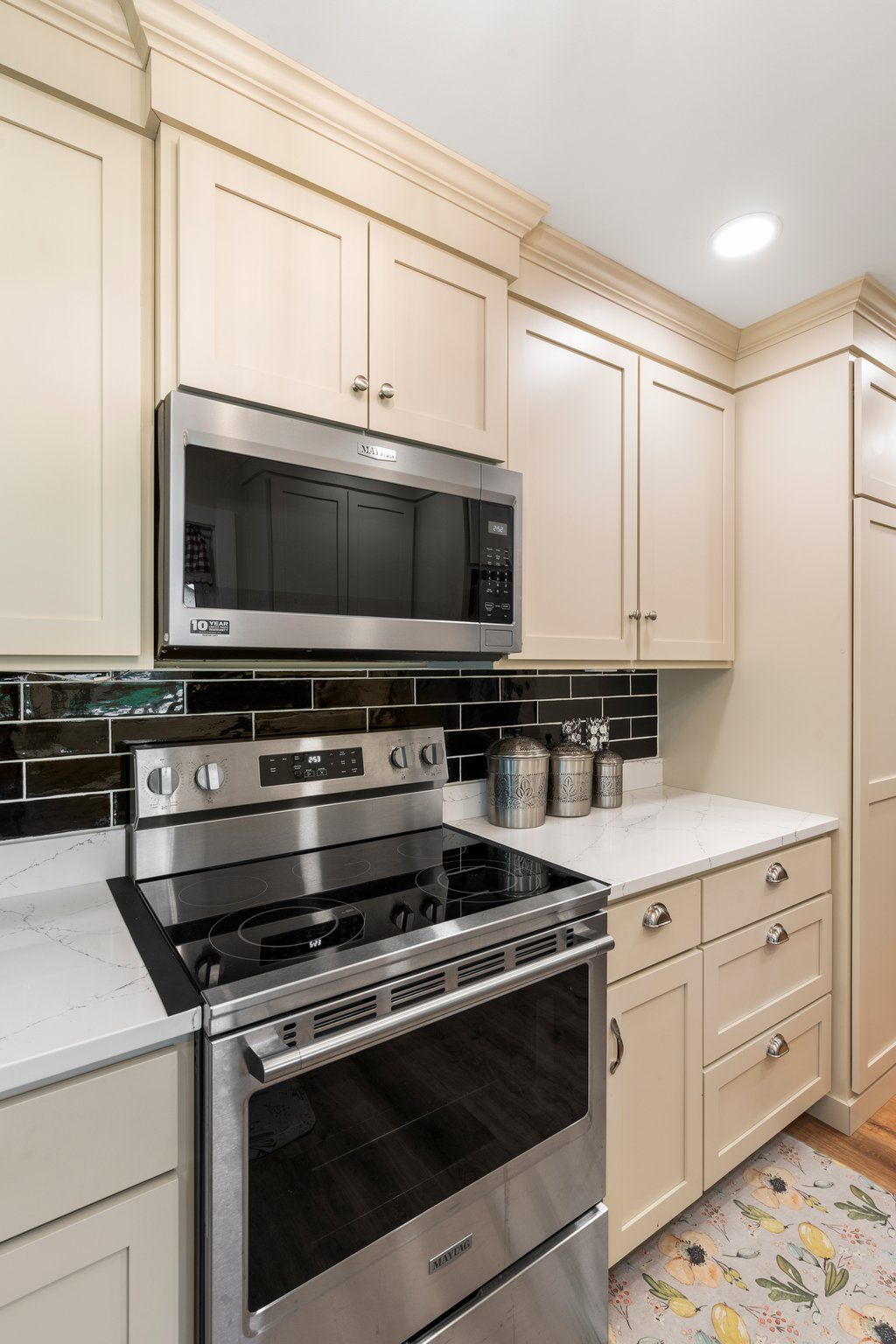 Kitchen with stainless steel range and microwave, light cabinets, black backsplash, and white countertops.
