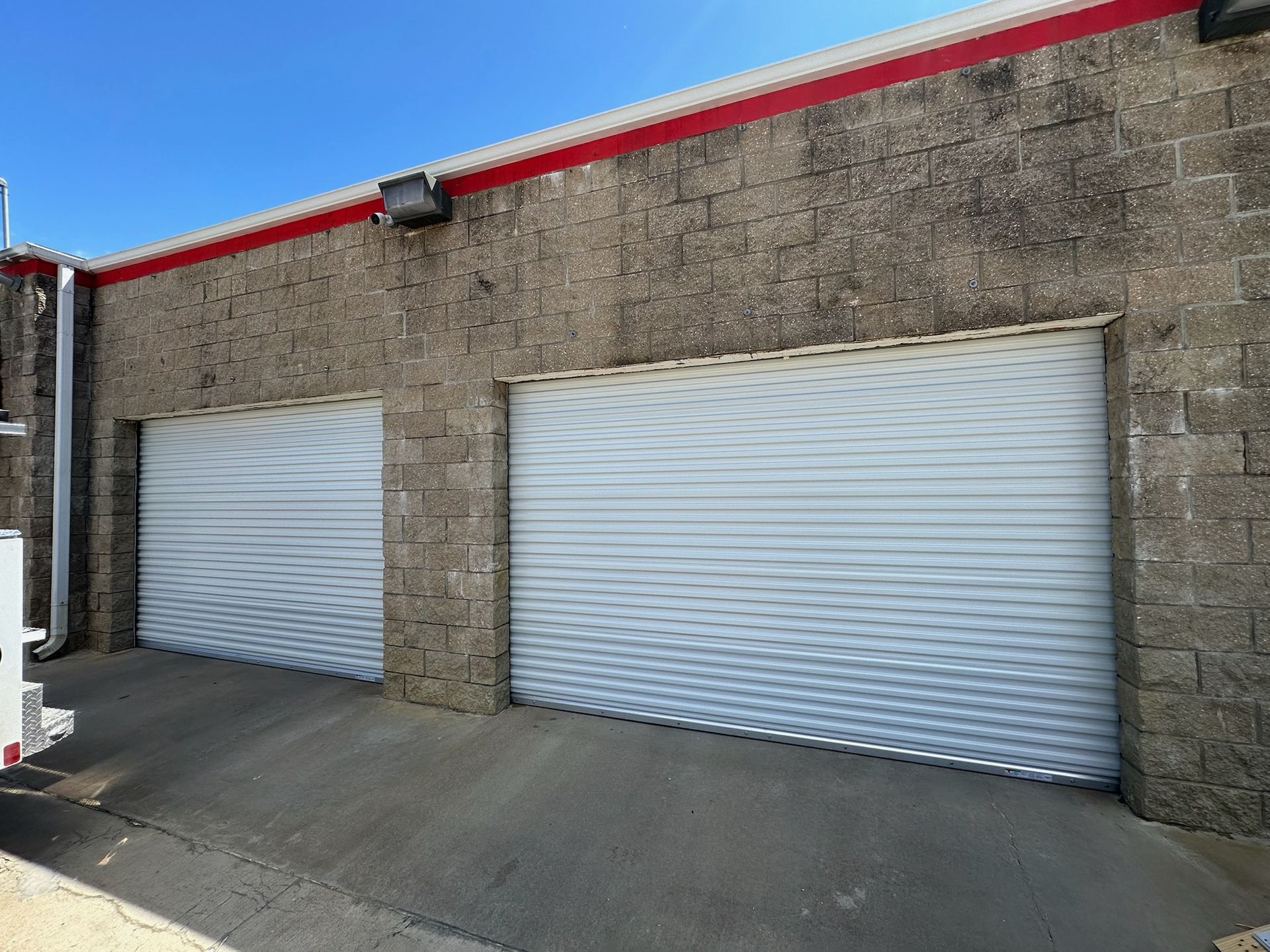 Two white roll-up garage doors on a brick industrial building under a clear blue sky