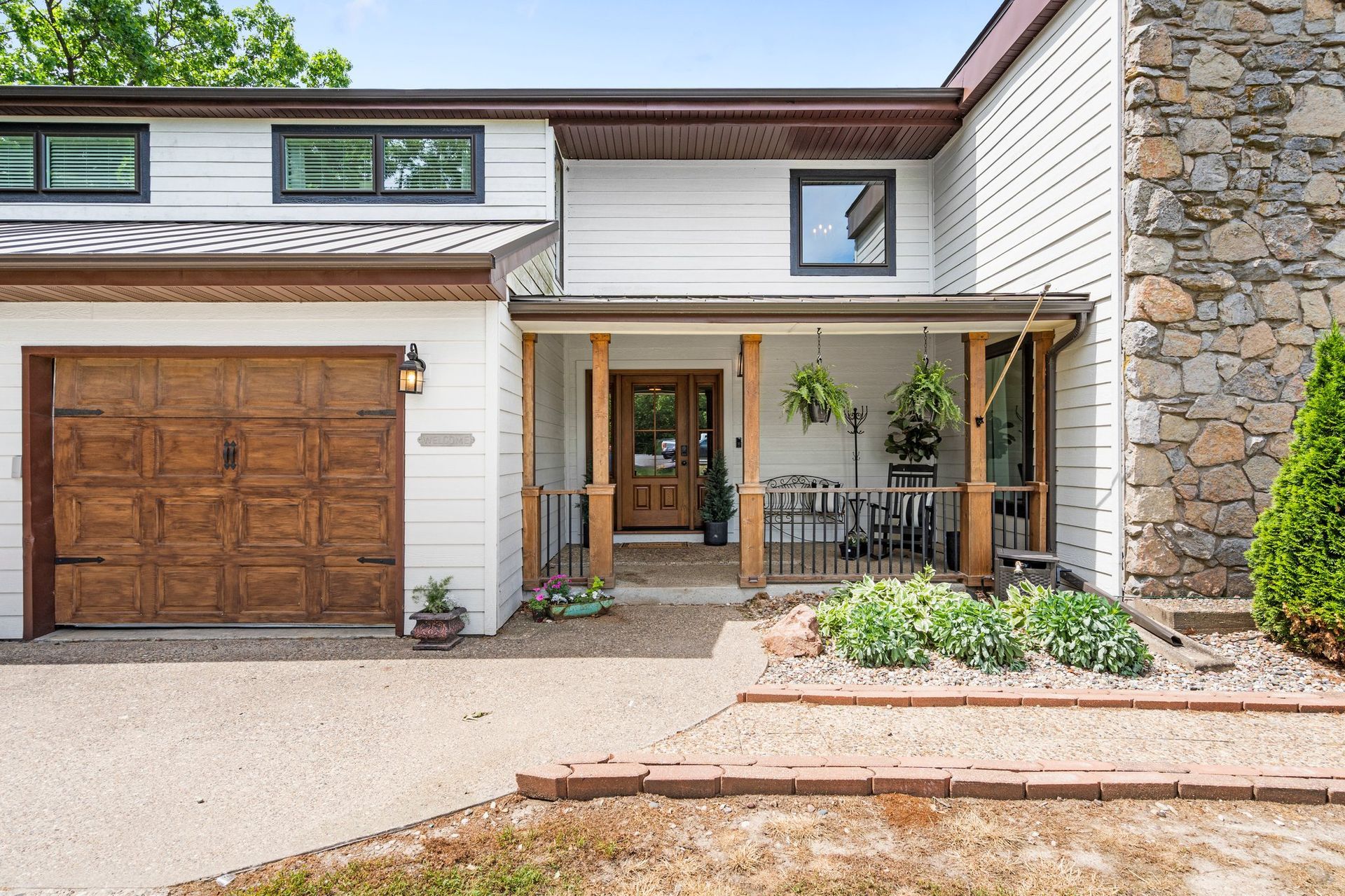 Two-story house with a brown garage door, wooden front porch, and stone chimney.