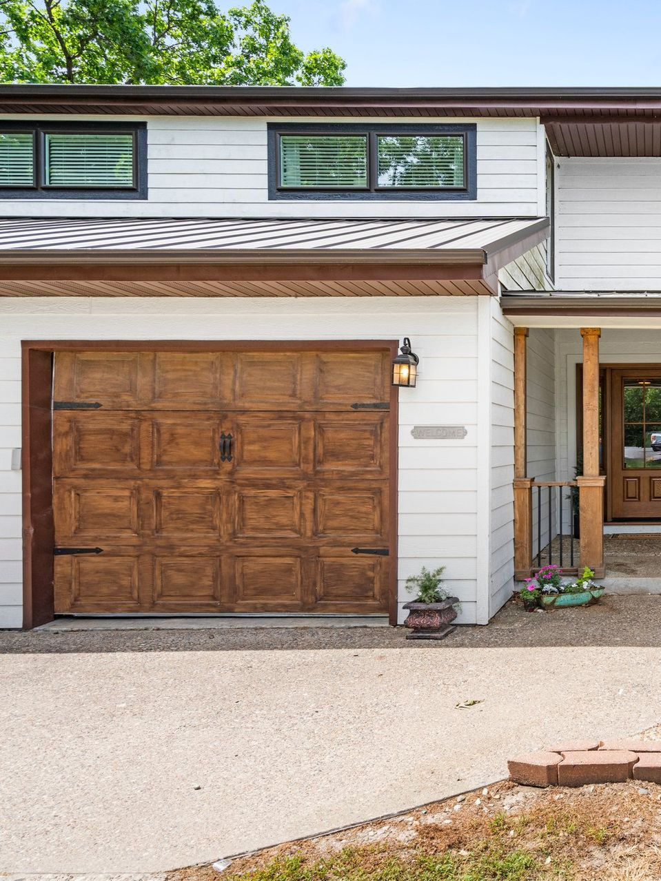 White house with a brown wooden garage door, small windows, and a gravel driveway.