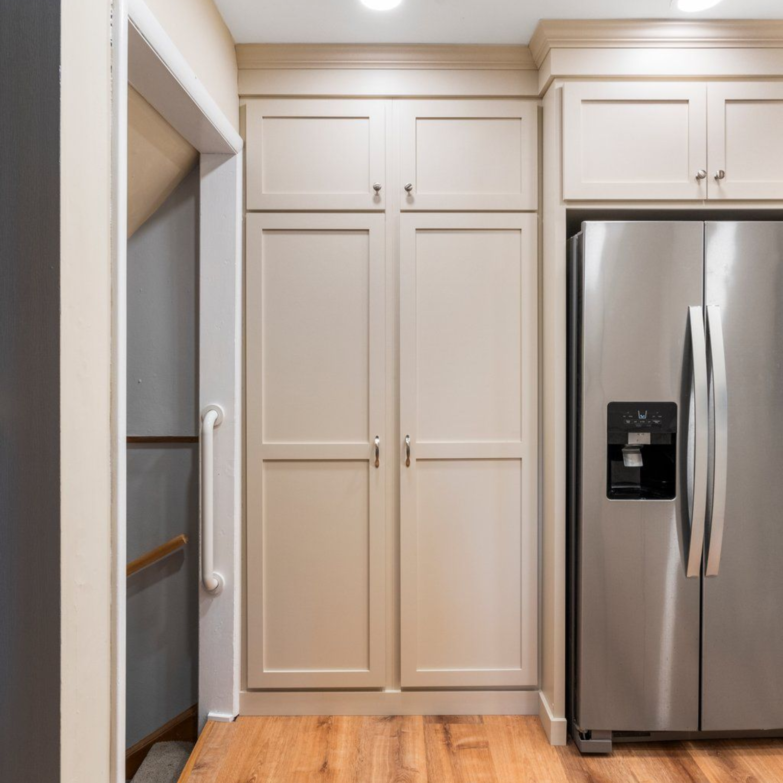 Kitchen with beige cabinets, stainless steel refrigerator, and entrance to staircase on the left.