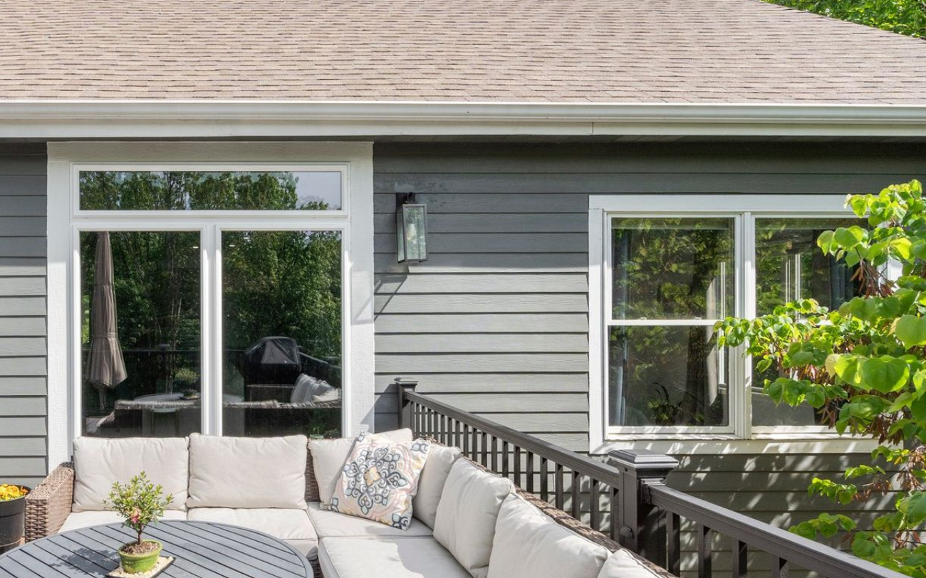 Backyard deck with a gray house, windows, and outdoor furniture.