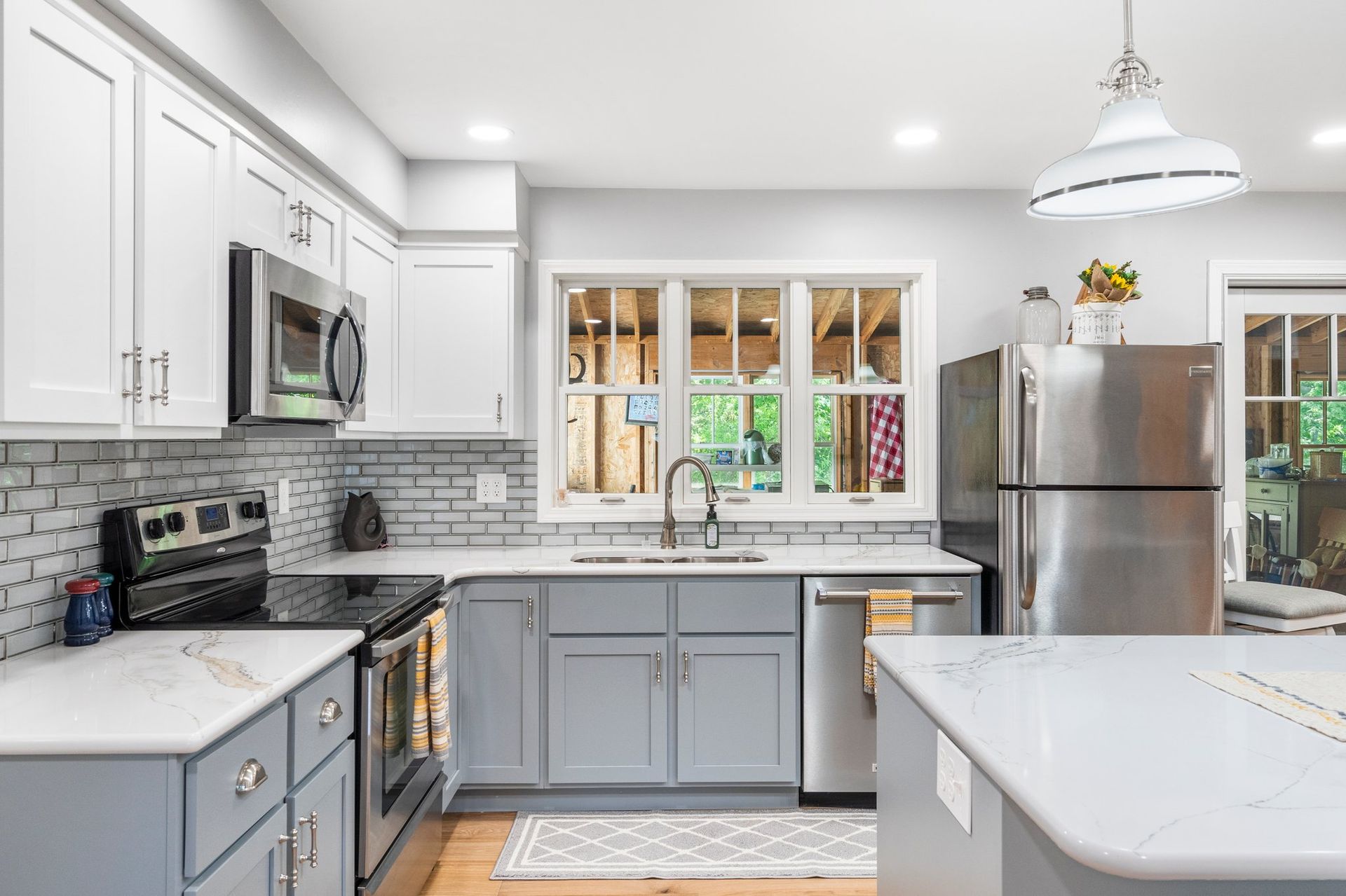 Kitchen with gray and white cabinets, stainless steel appliances, and a window overlooking a porch.