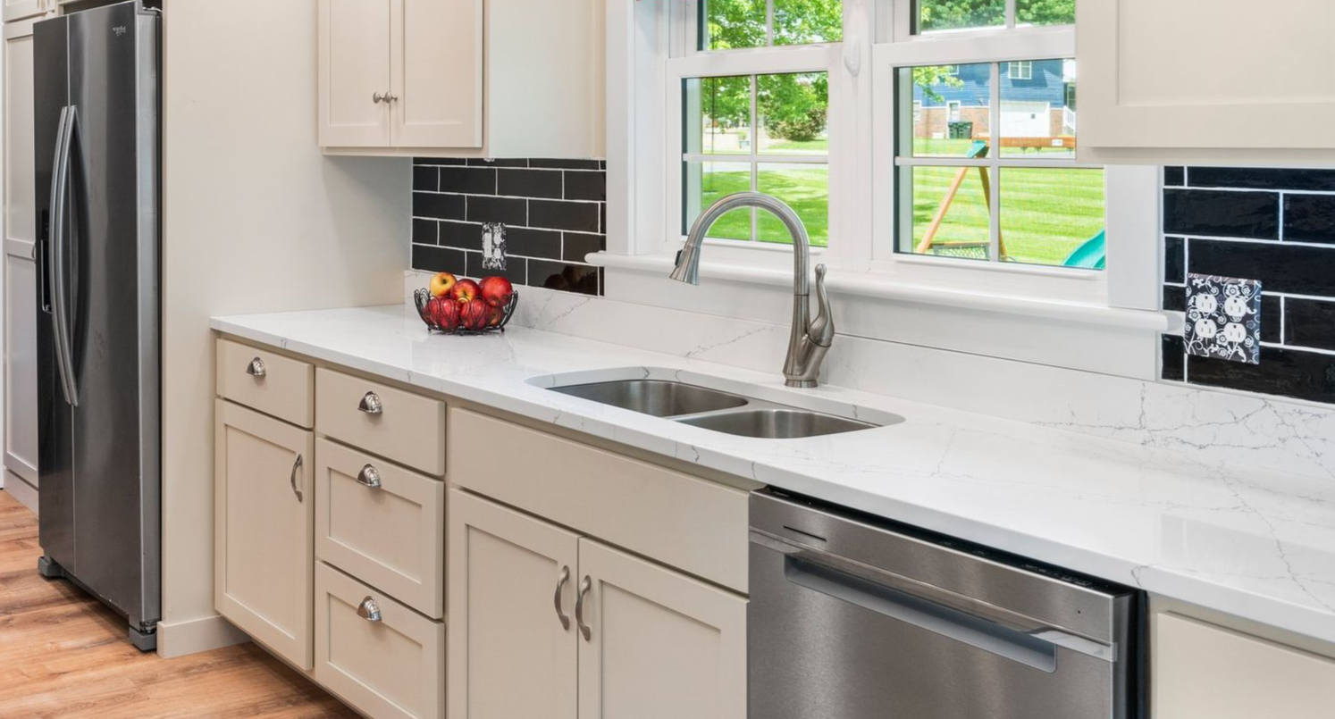 Kitchen with white cabinets, stainless steel appliances, white countertop, black tile backsplash, and window.