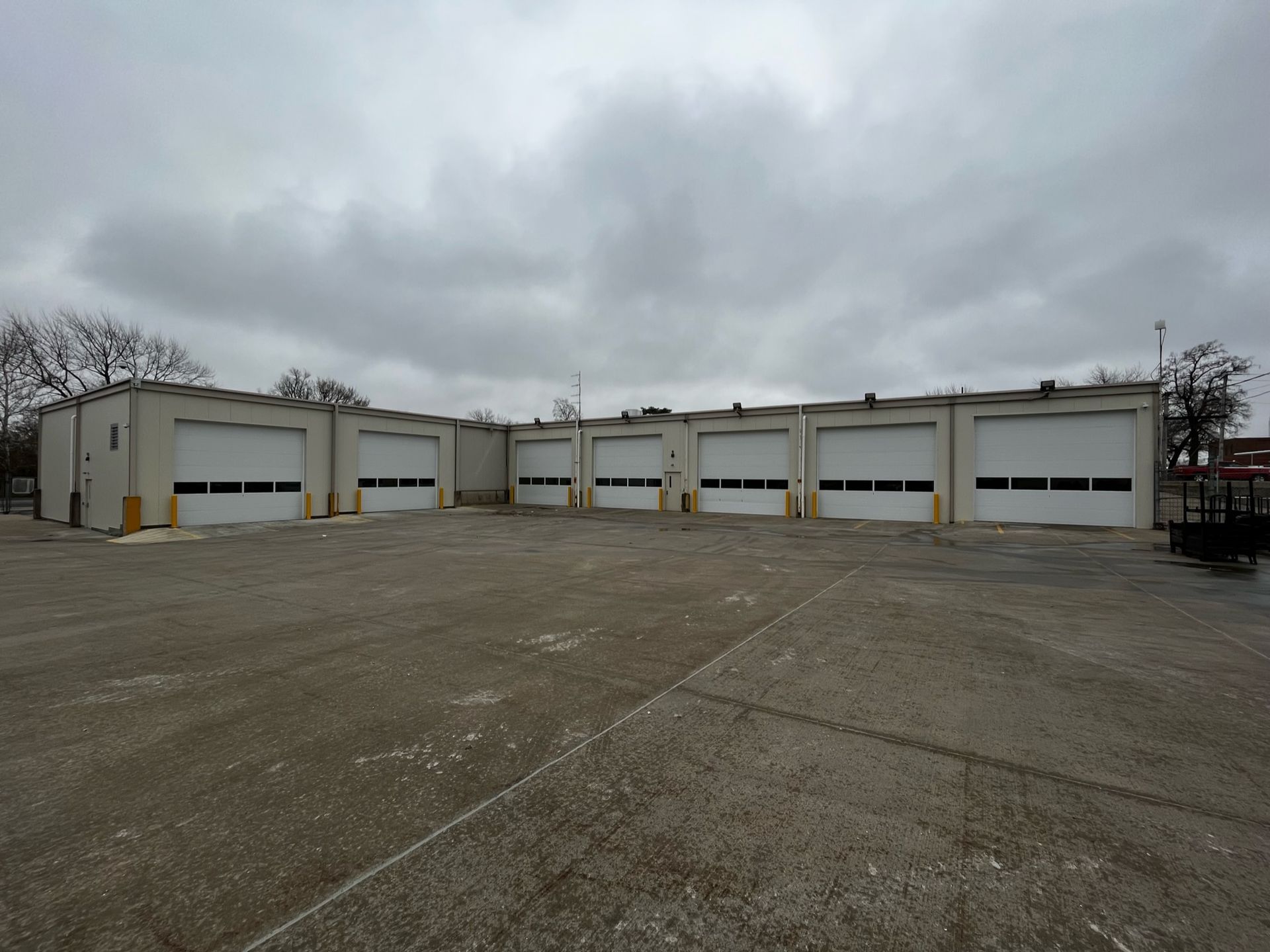 White commercial building with multiple garage doors under a cloudy sky.