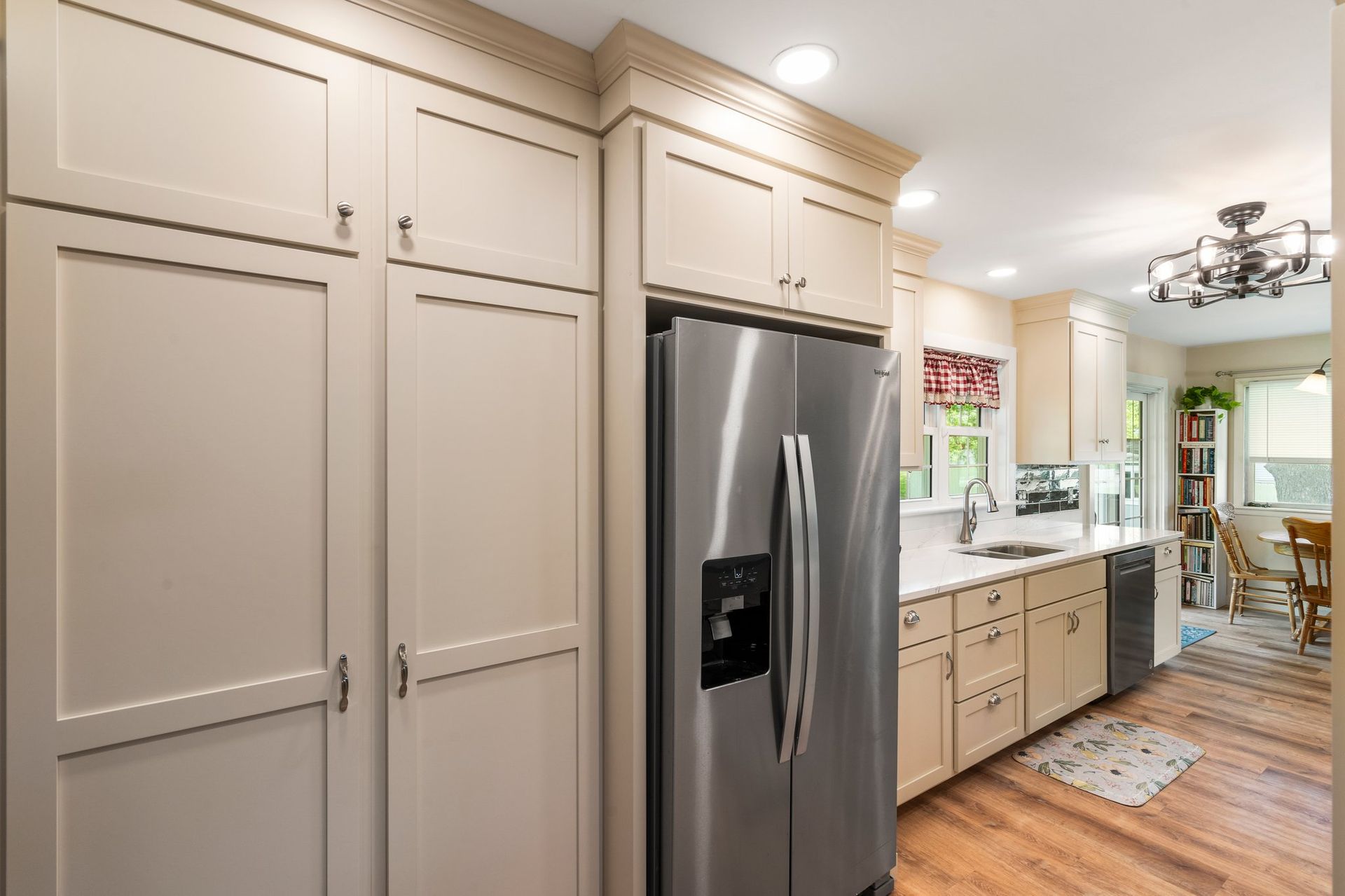 A traditional kitchen with cream cabinets and a silver fridge. 