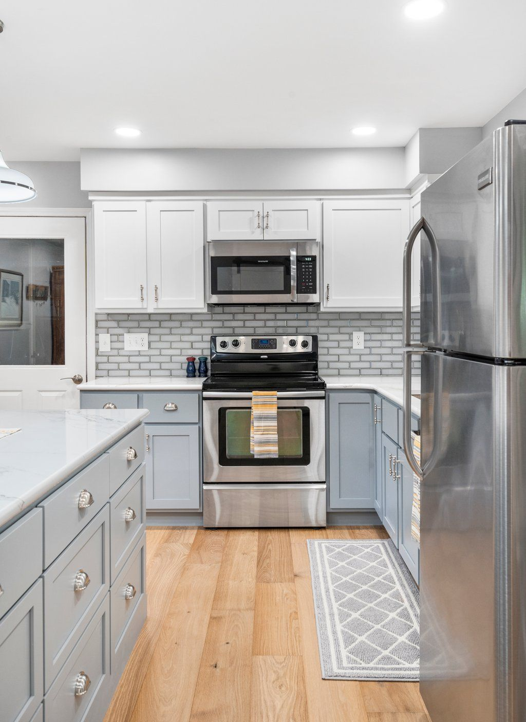 Modern kitchen with white and blue cabinets, stainless steel appliances, and wood flooring.