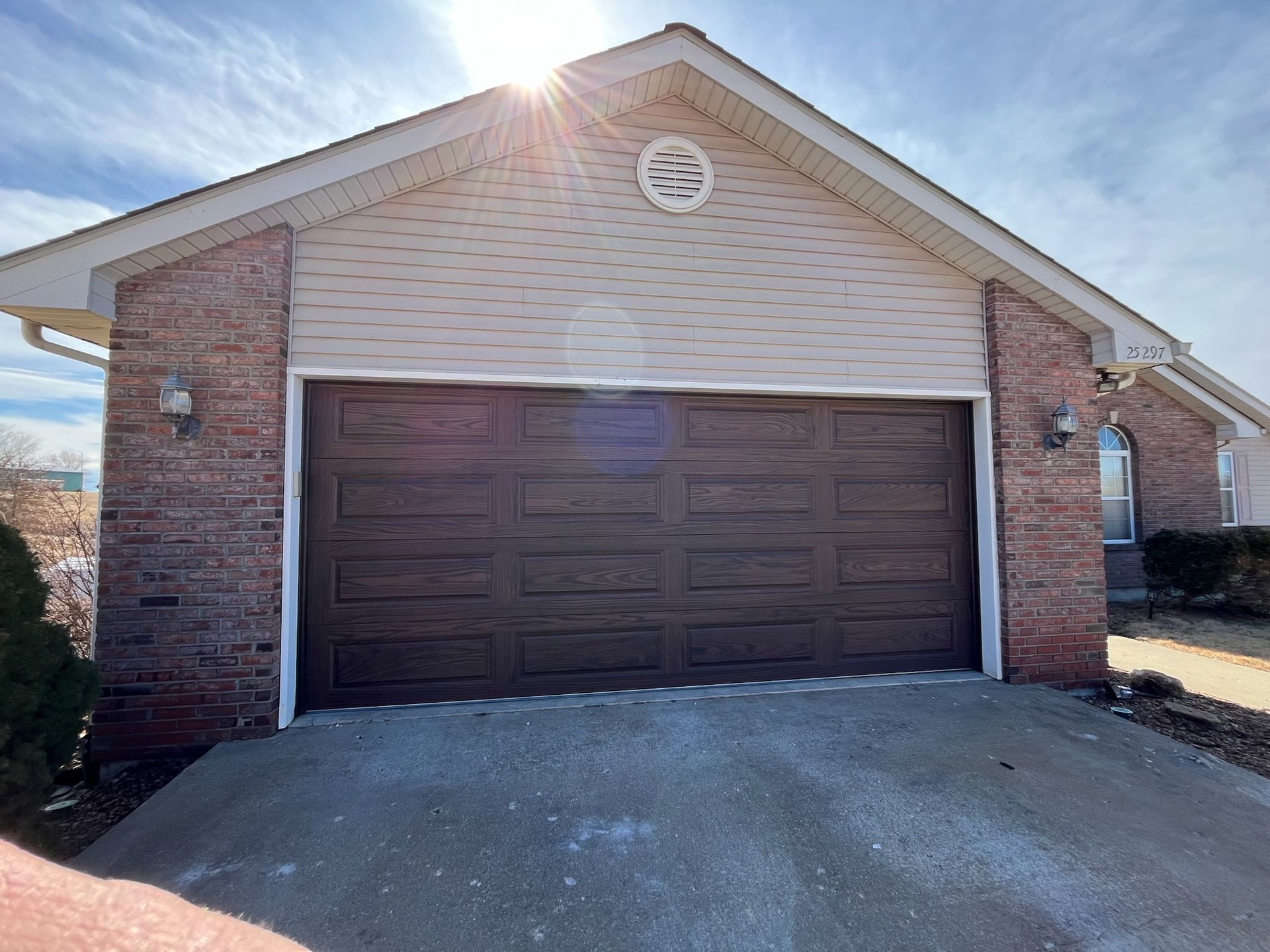 Brown garage door on a house with brick and tan siding. Sunny day. Concrete driveway.