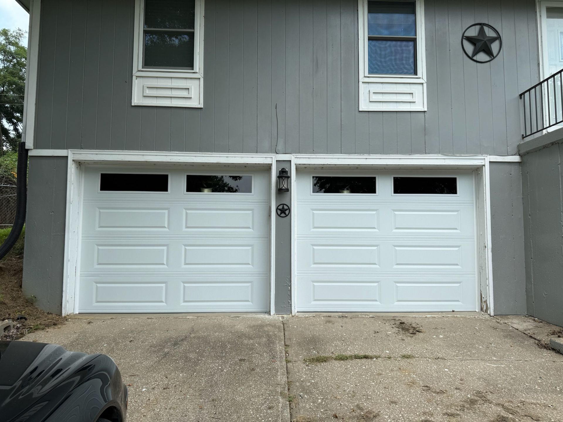 Two white garage doors with windows, gray siding, and a concrete driveway.