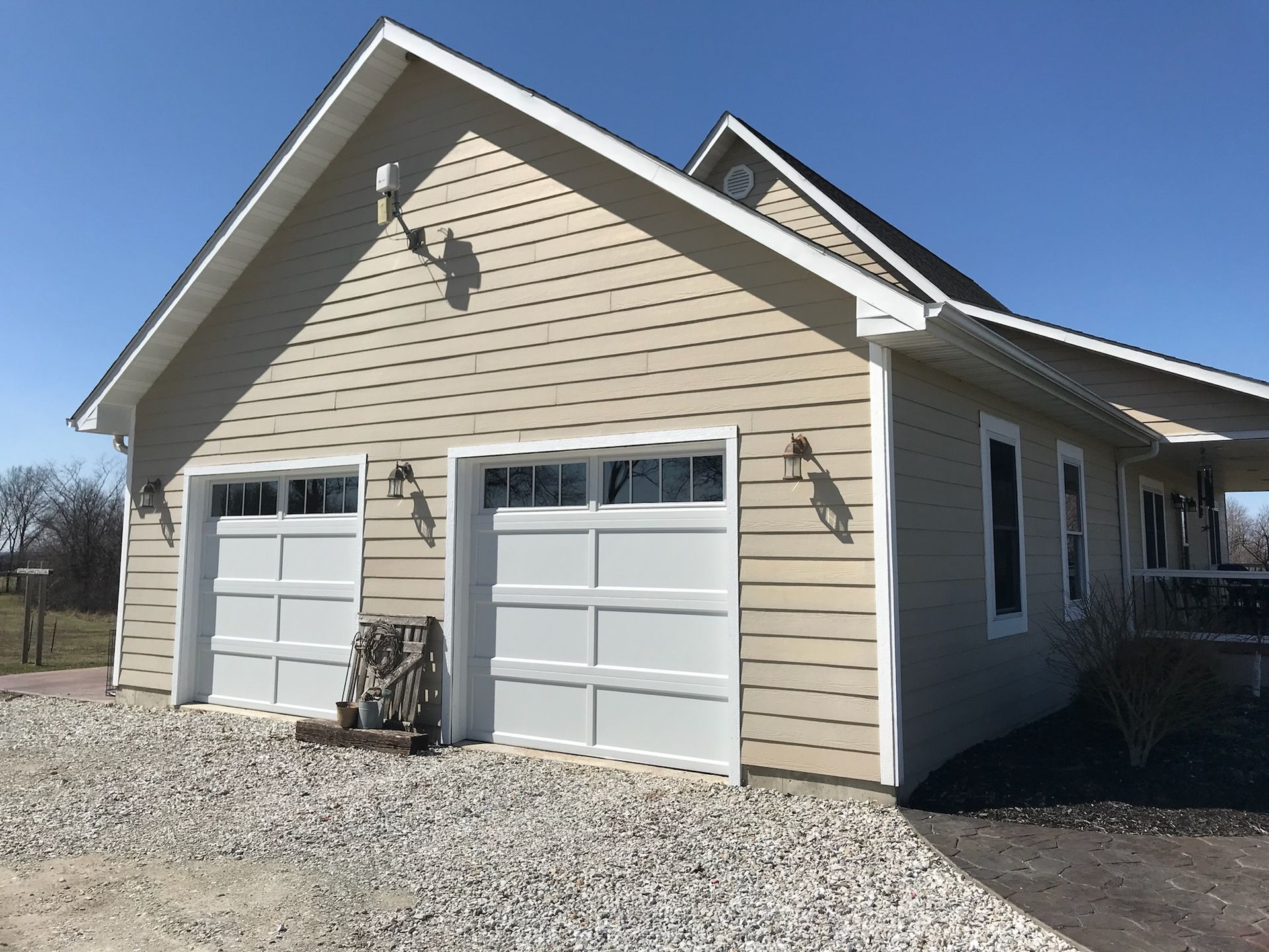 Beige detached garage with two white doors and gravel driveway under a blue sky