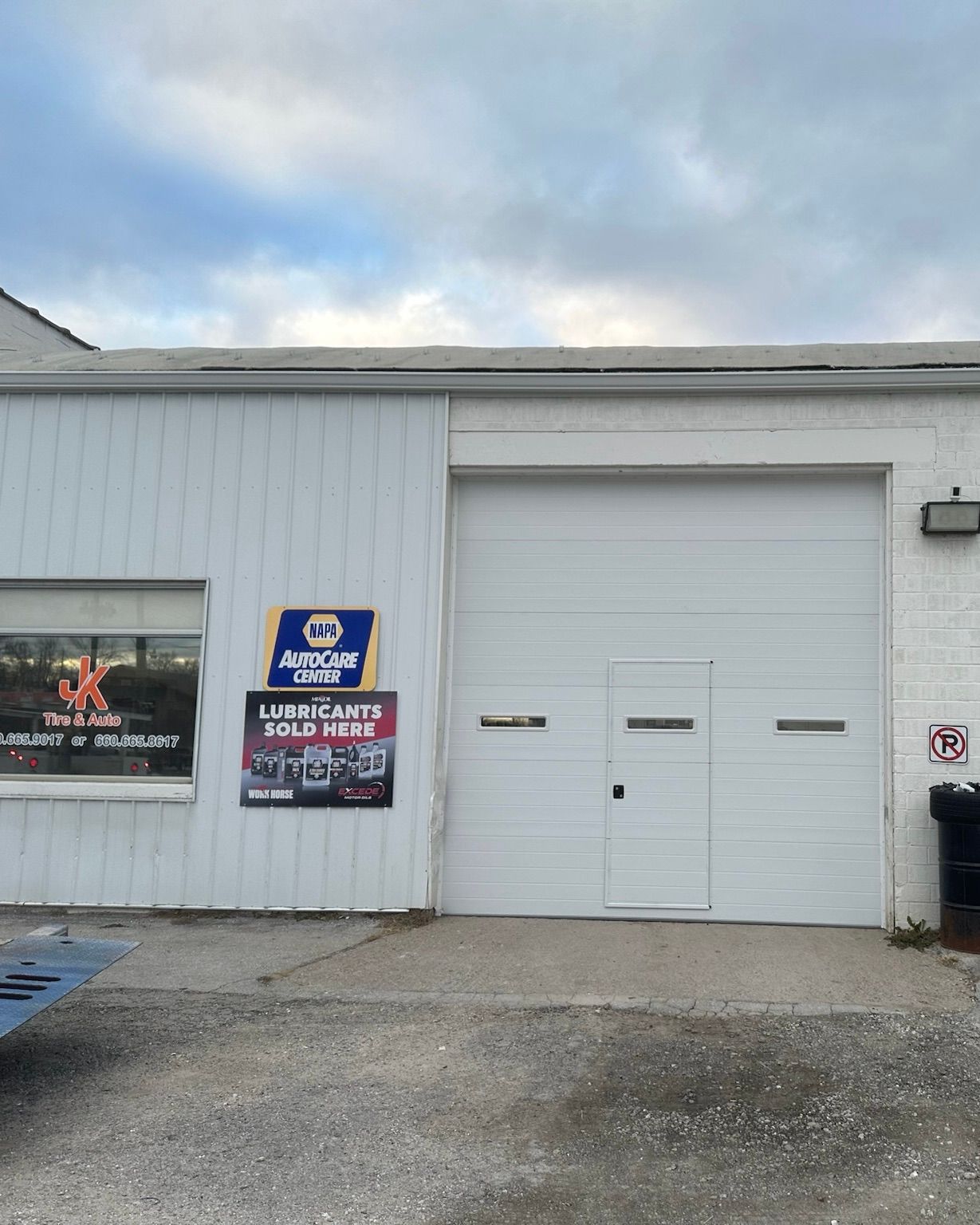 White industrial building exterior with a garage door and store signs under an overcast sky