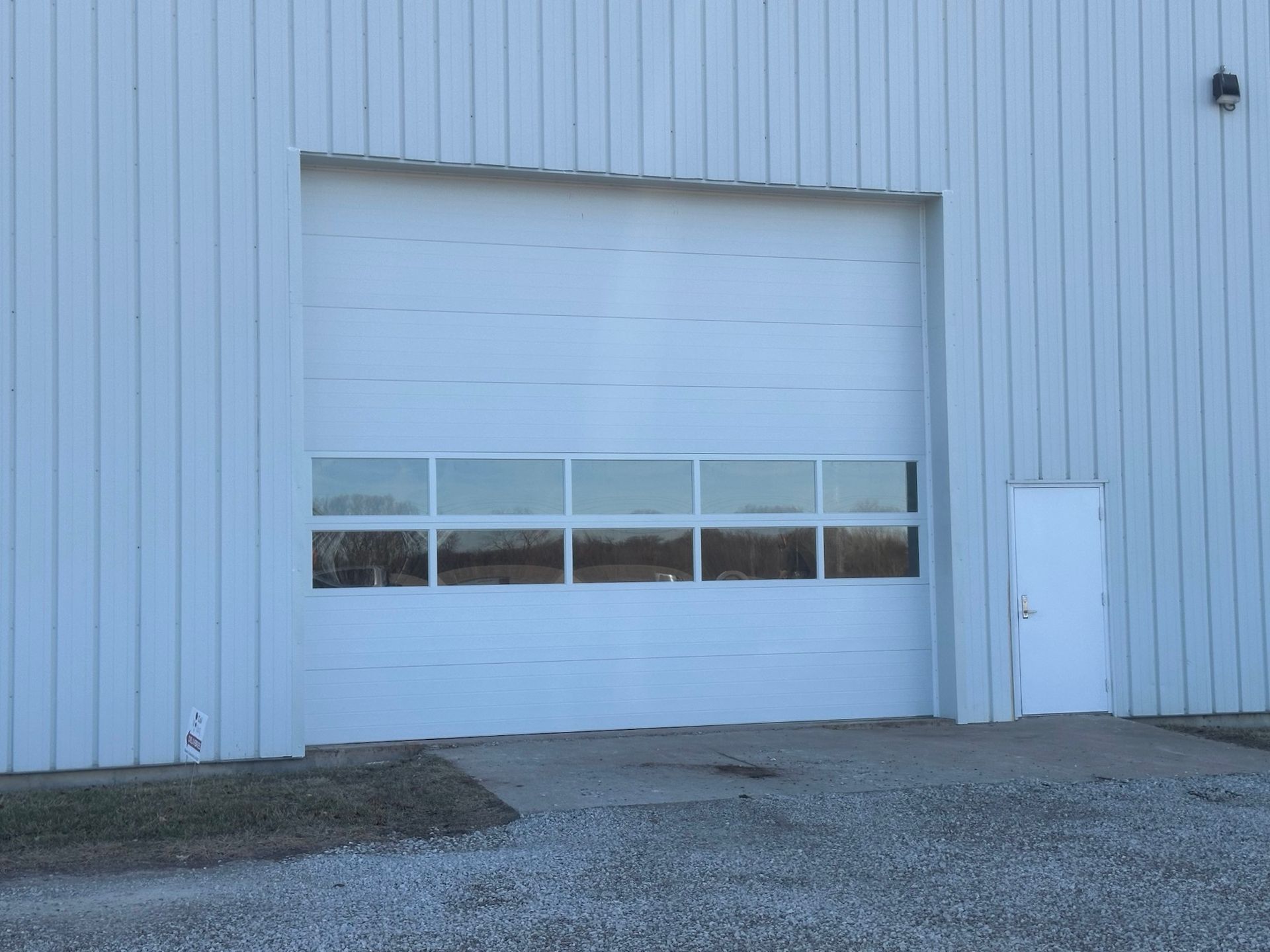 White industrial building wall with a closed garage door and gravel lot in front