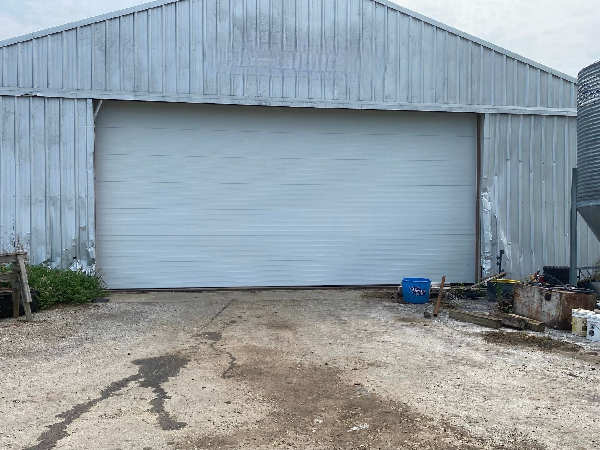 White barn with closed overhead door; gravel ground in front.
