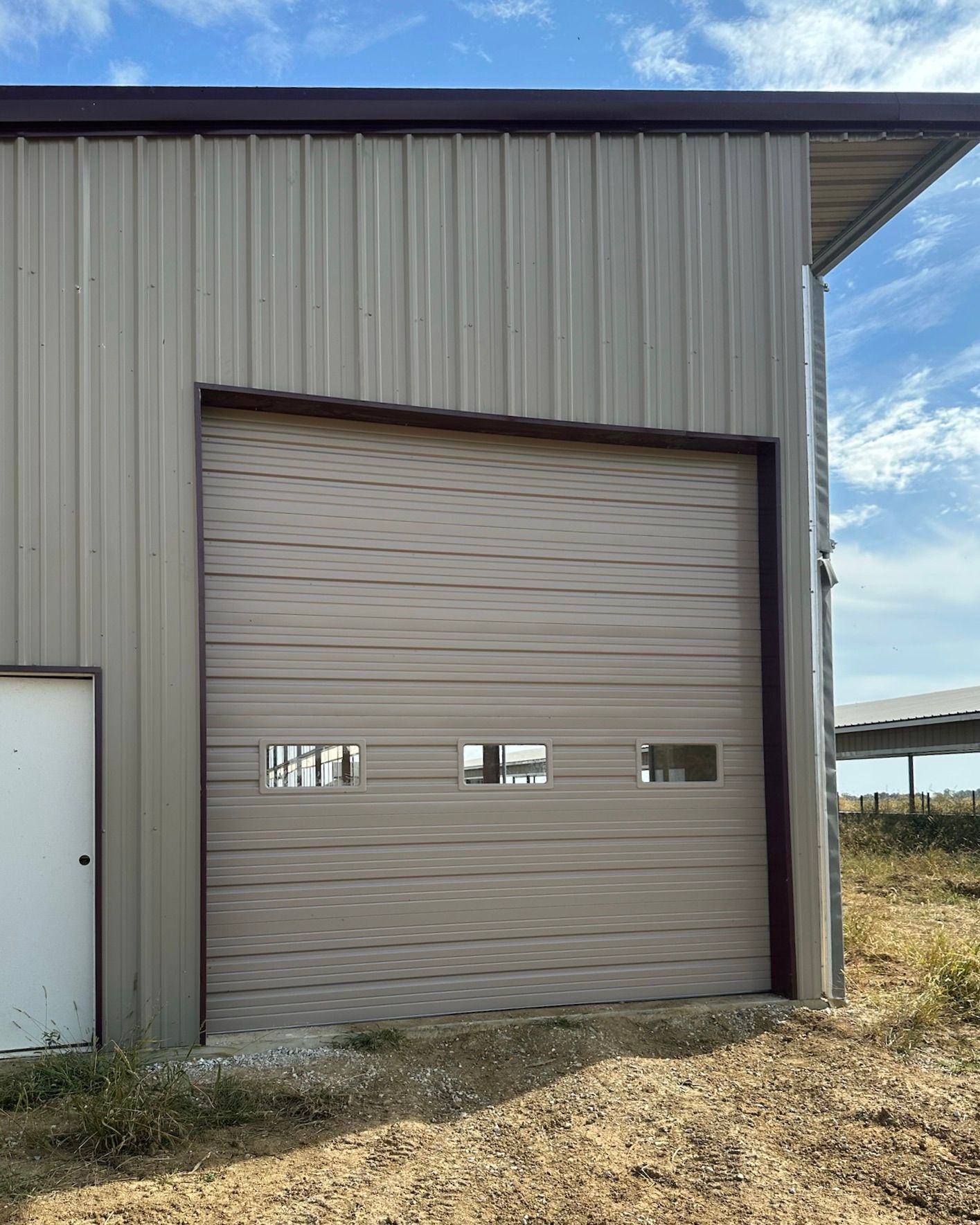 Closed beige industrial garage door on a metal building under a blue sky.