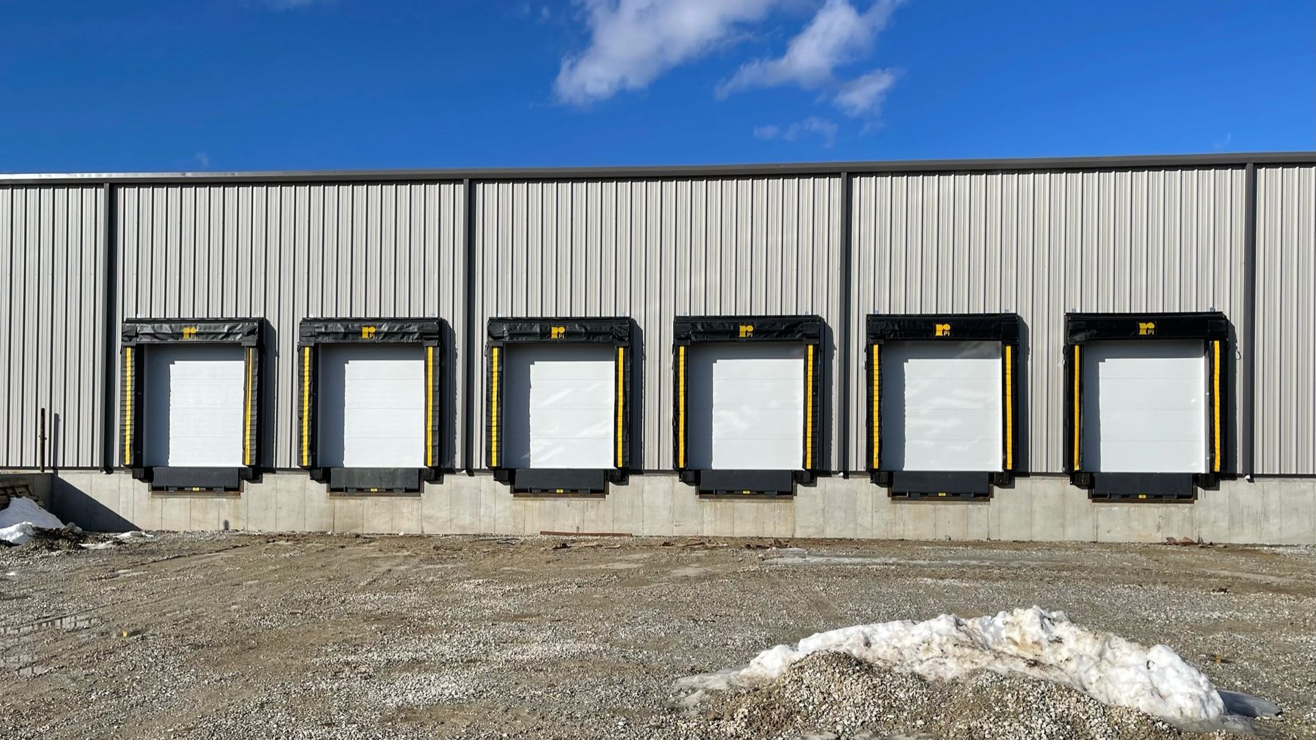 Six loading dock doors on a gray industrial building under a blue sky.