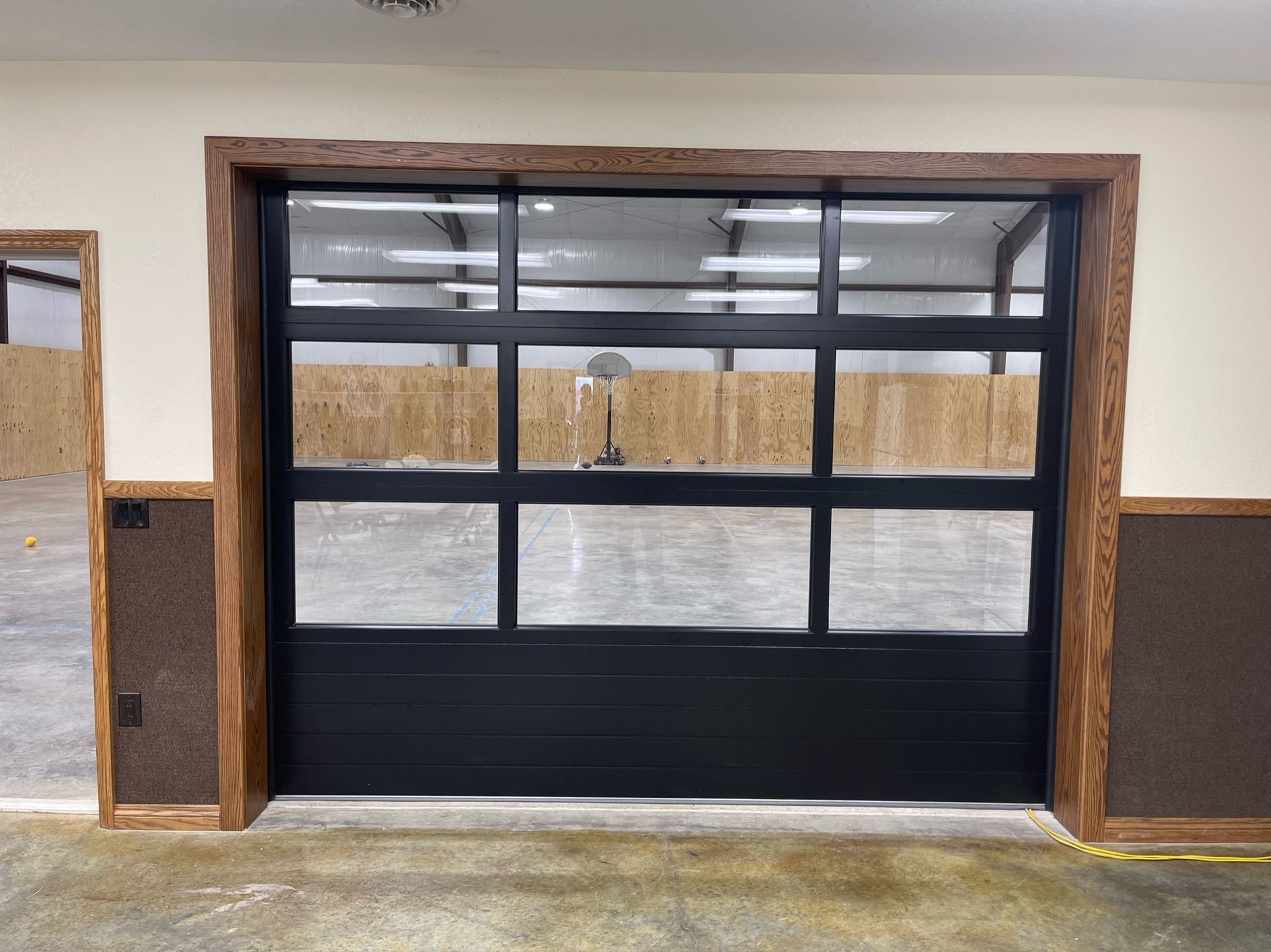 Black glass garage door with wooden frame and interior view of a basketball court.