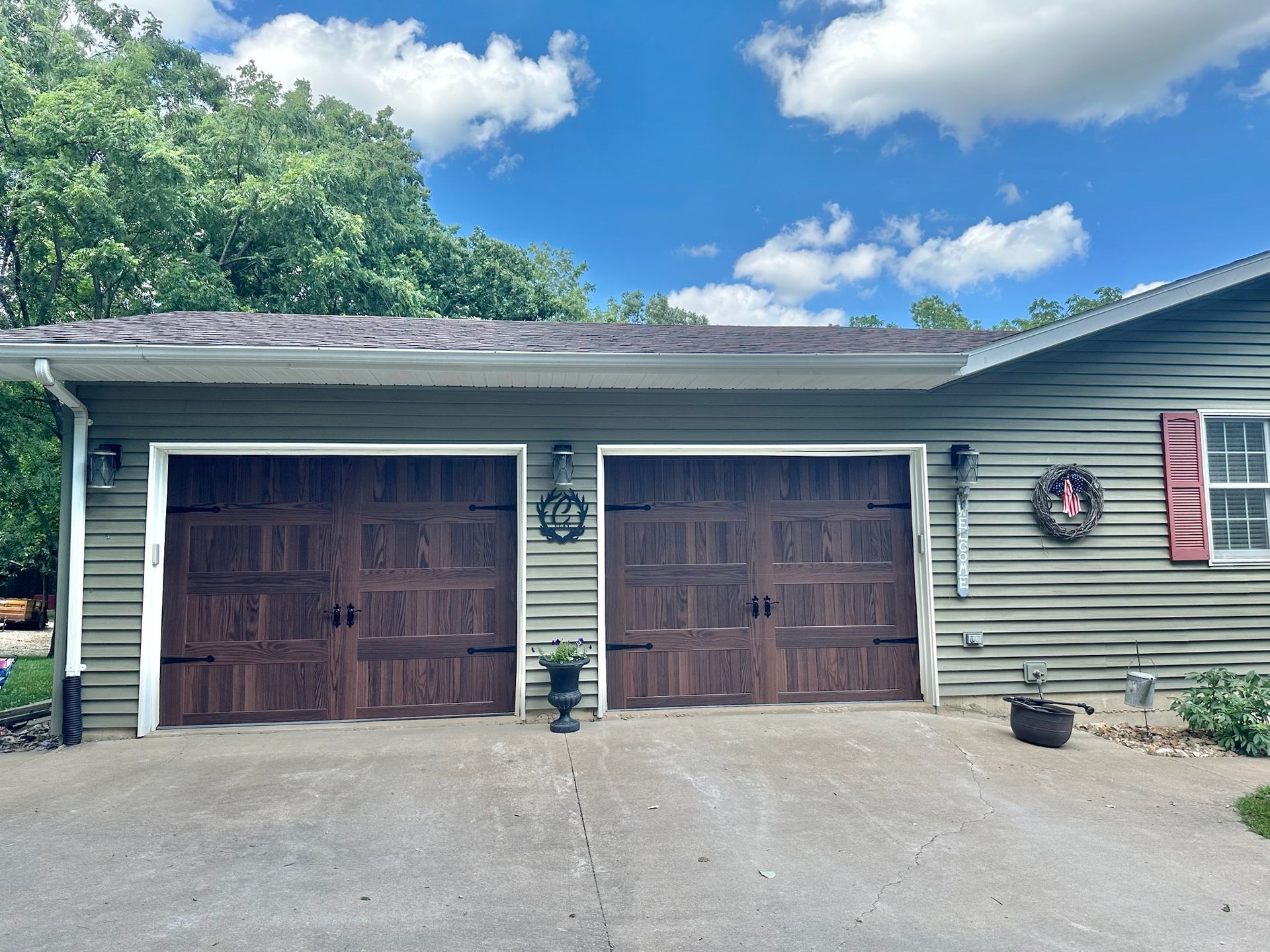 Two-car garage with brown wooden doors, green siding, and a blue sky background.