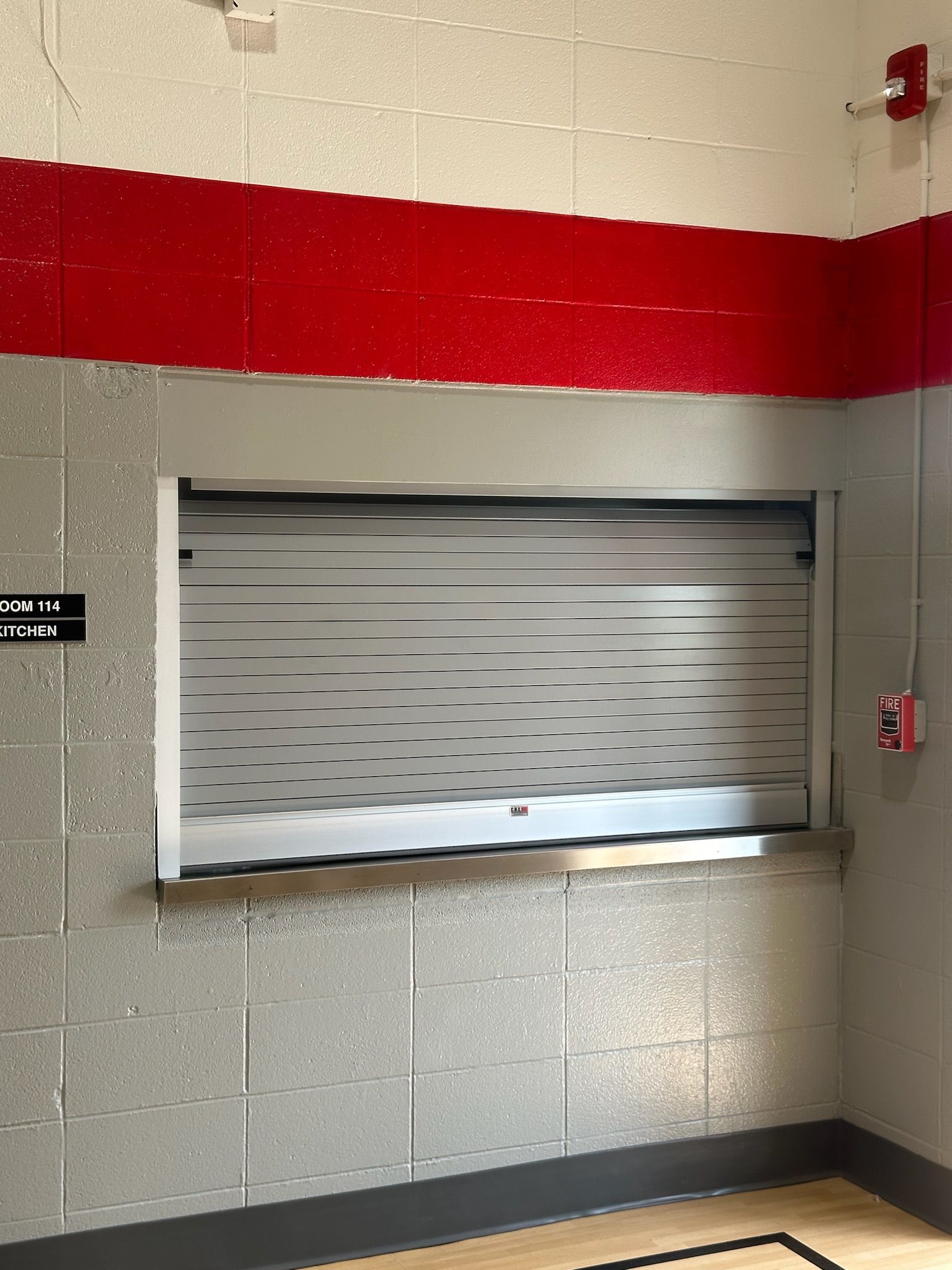 Closed concession stand window with a red stripe above it. Gray brick wall.