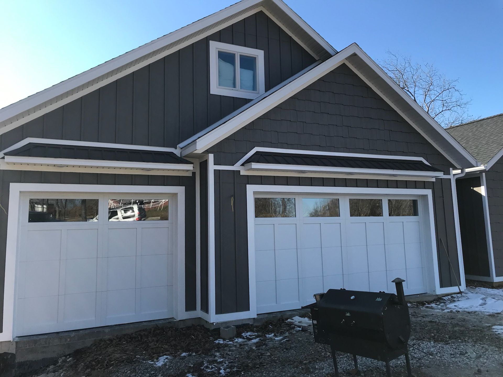 Two-car garage with gray siding, white trim, and white garage doors. A window is in the gable above the doors.
