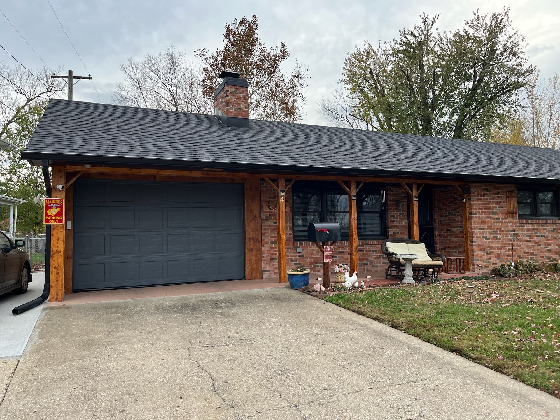 Brick house with dark roof, gray garage door, front porch, and driveway under an overcast sky