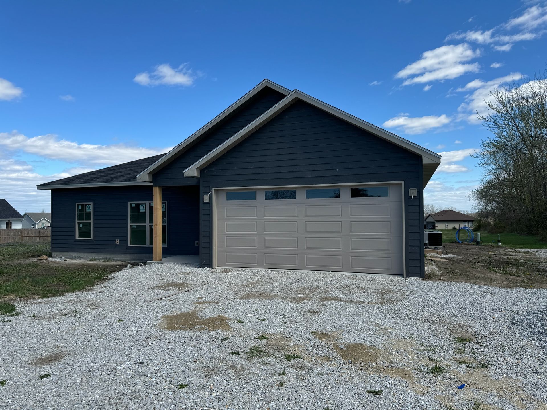 Blue-sided house with a tan garage door on a gravel driveway under a partly cloudy sky.