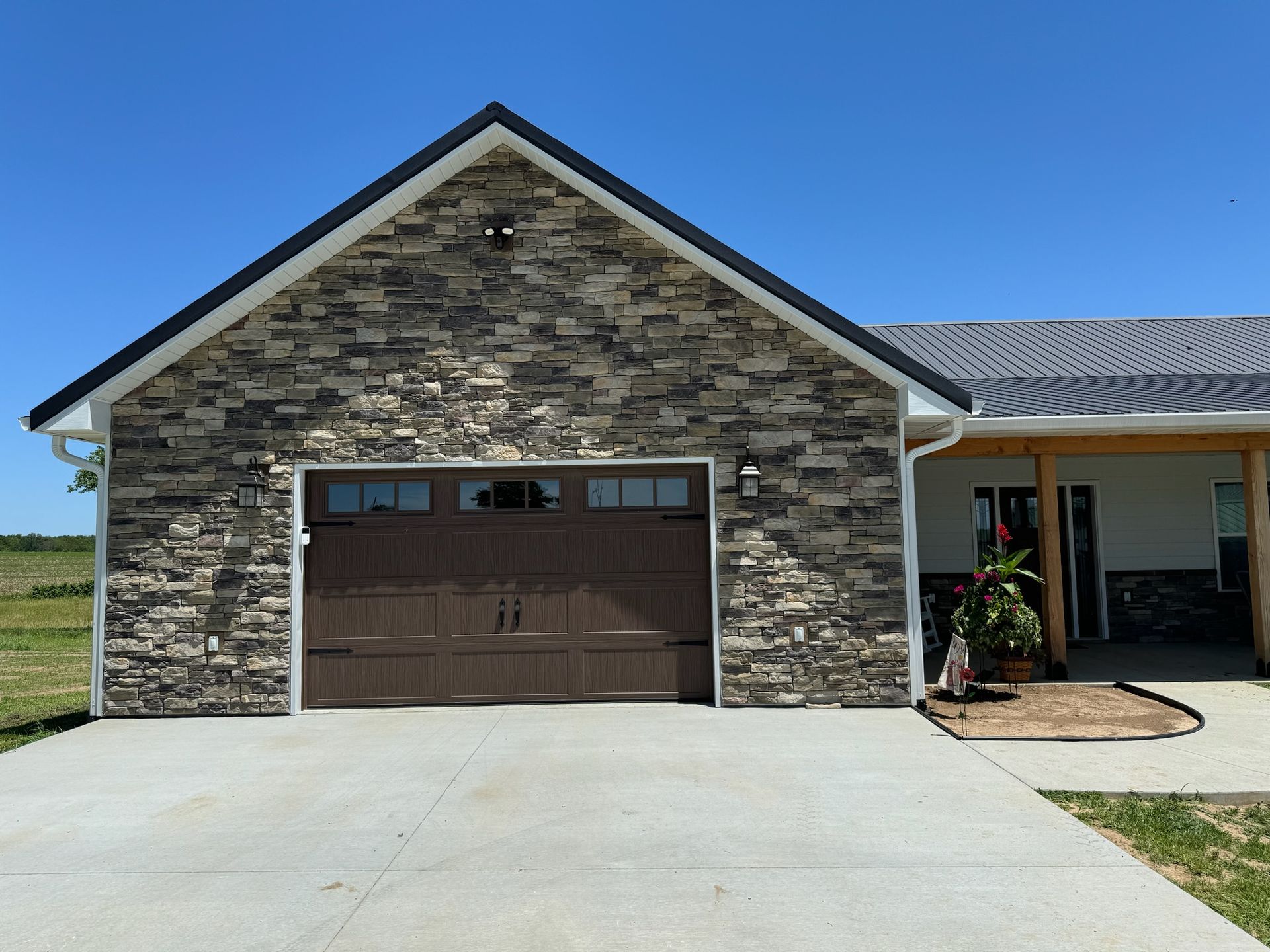 Single-car garage with stone facade and brown door on a house under a clear blue sky