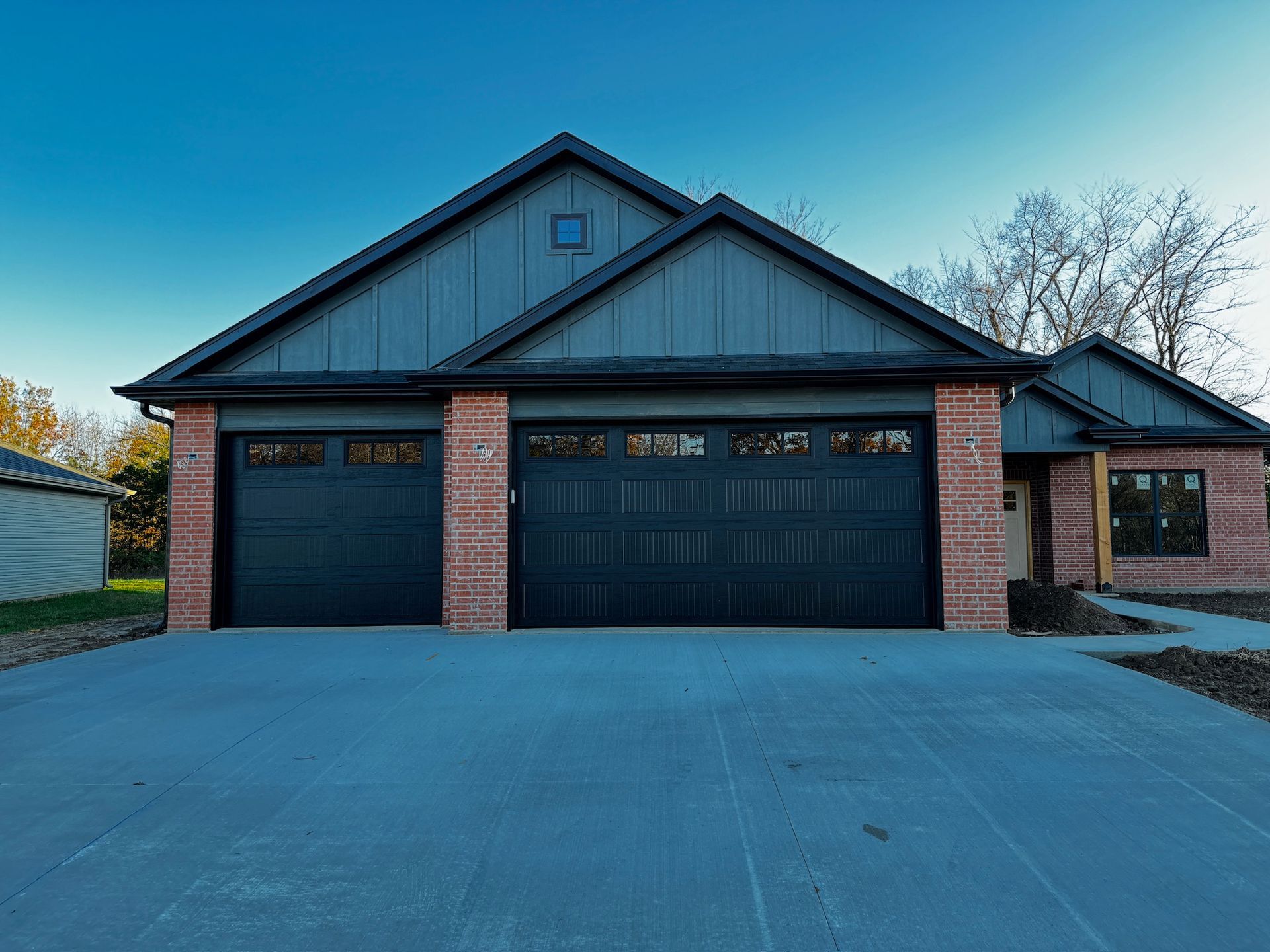 Suburban brick house with a three-car garage and dark gray roof at dusk