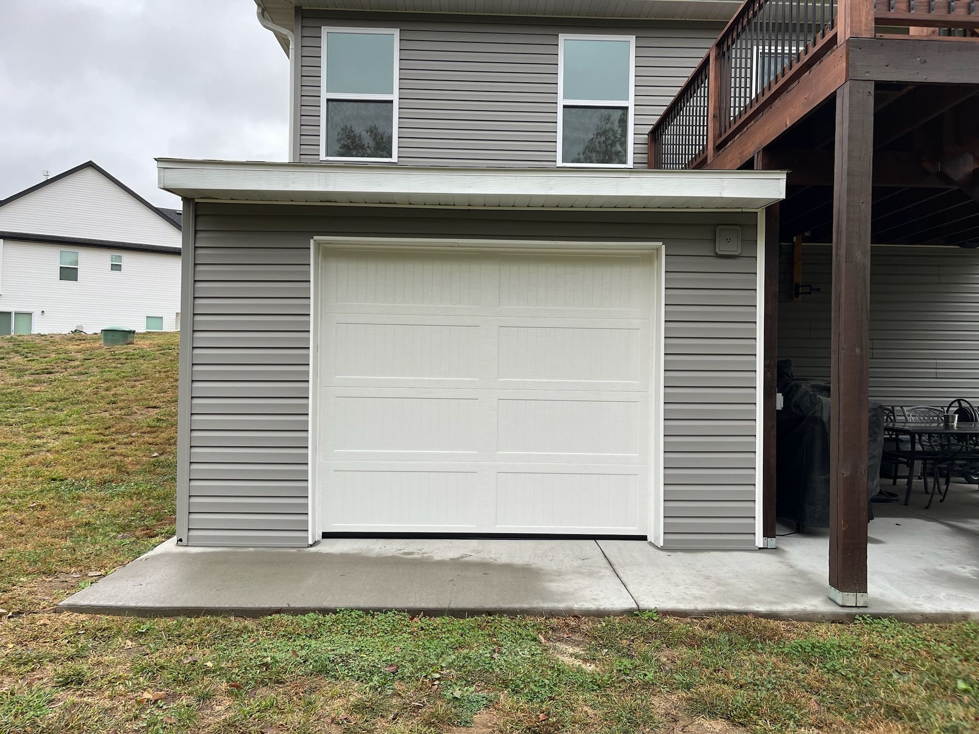 Small white garage with a closed door beside a house and concrete driveway