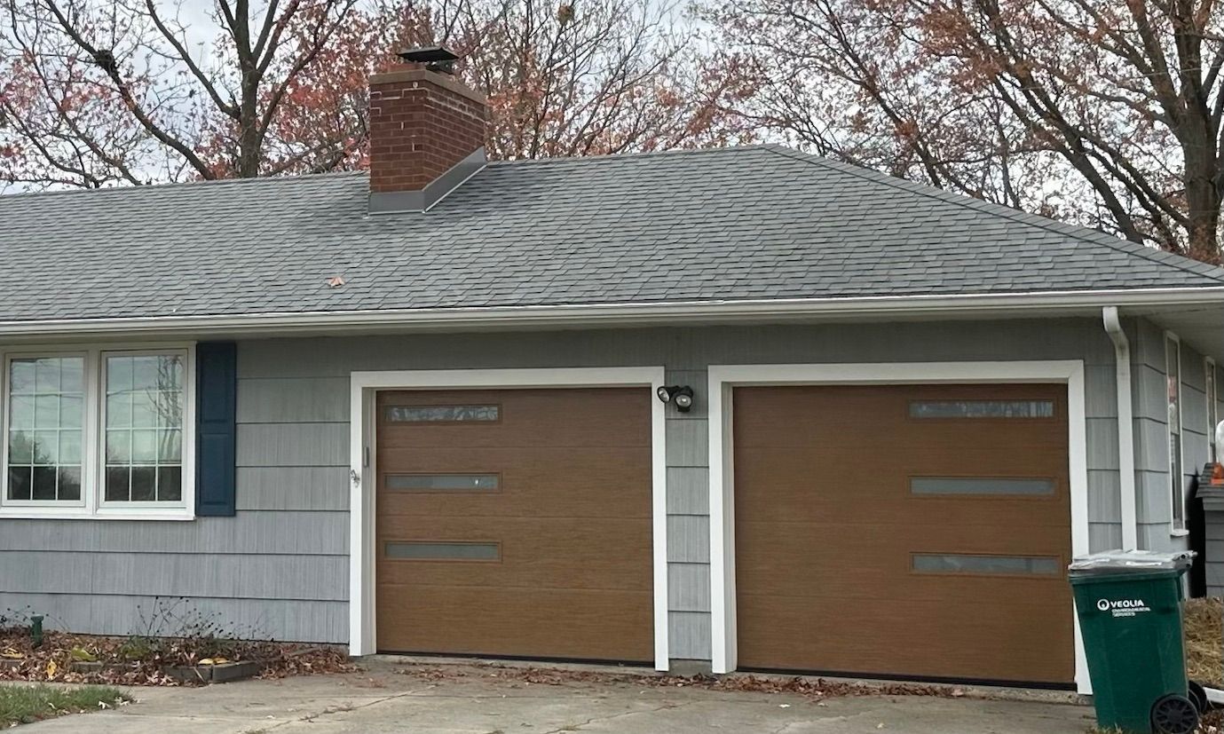 Two-car garage with brown doors and gray siding beneath a shingled roof